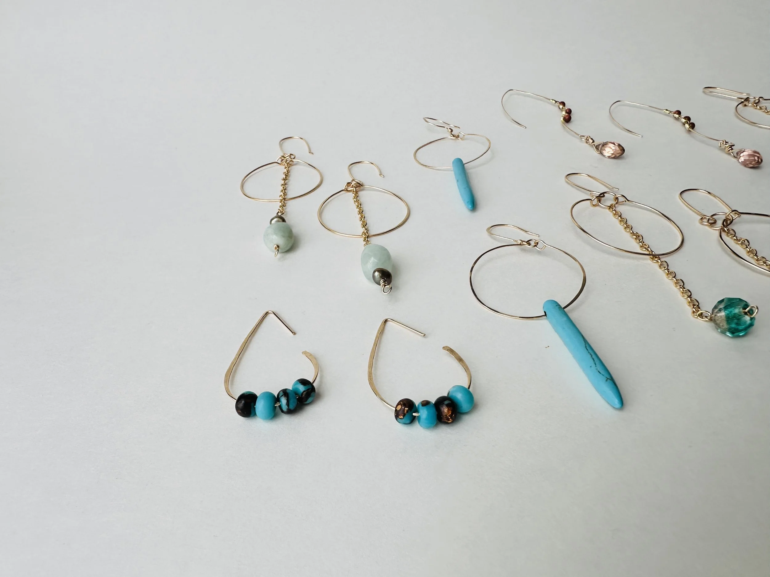 Collection of various earrings with beads and chains arranged on a light surface.