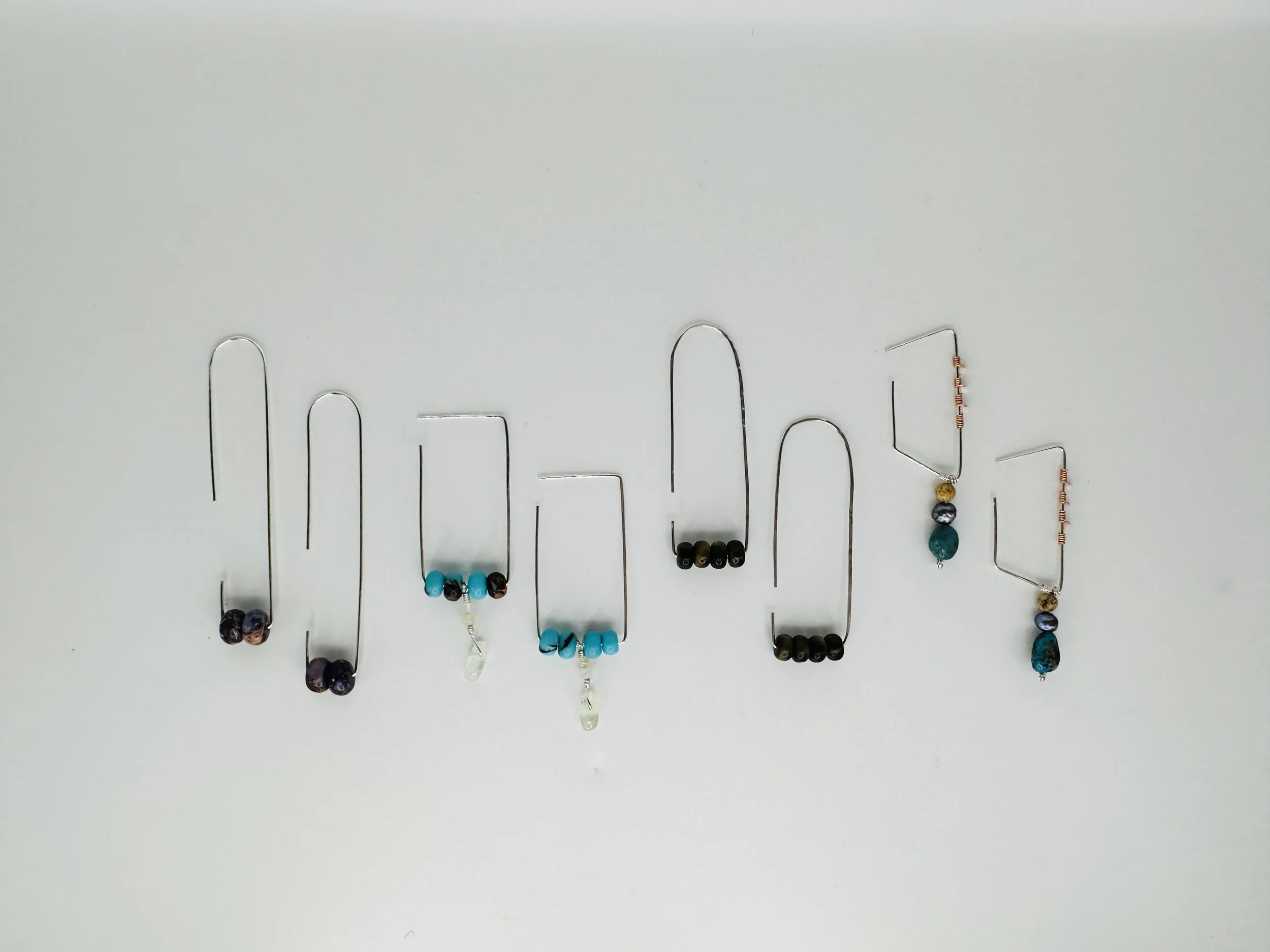A collection of jewelry featuring various beaded necklaces with different colored and shaped beads, displayed on a white background with the beads hanging from silver wires.