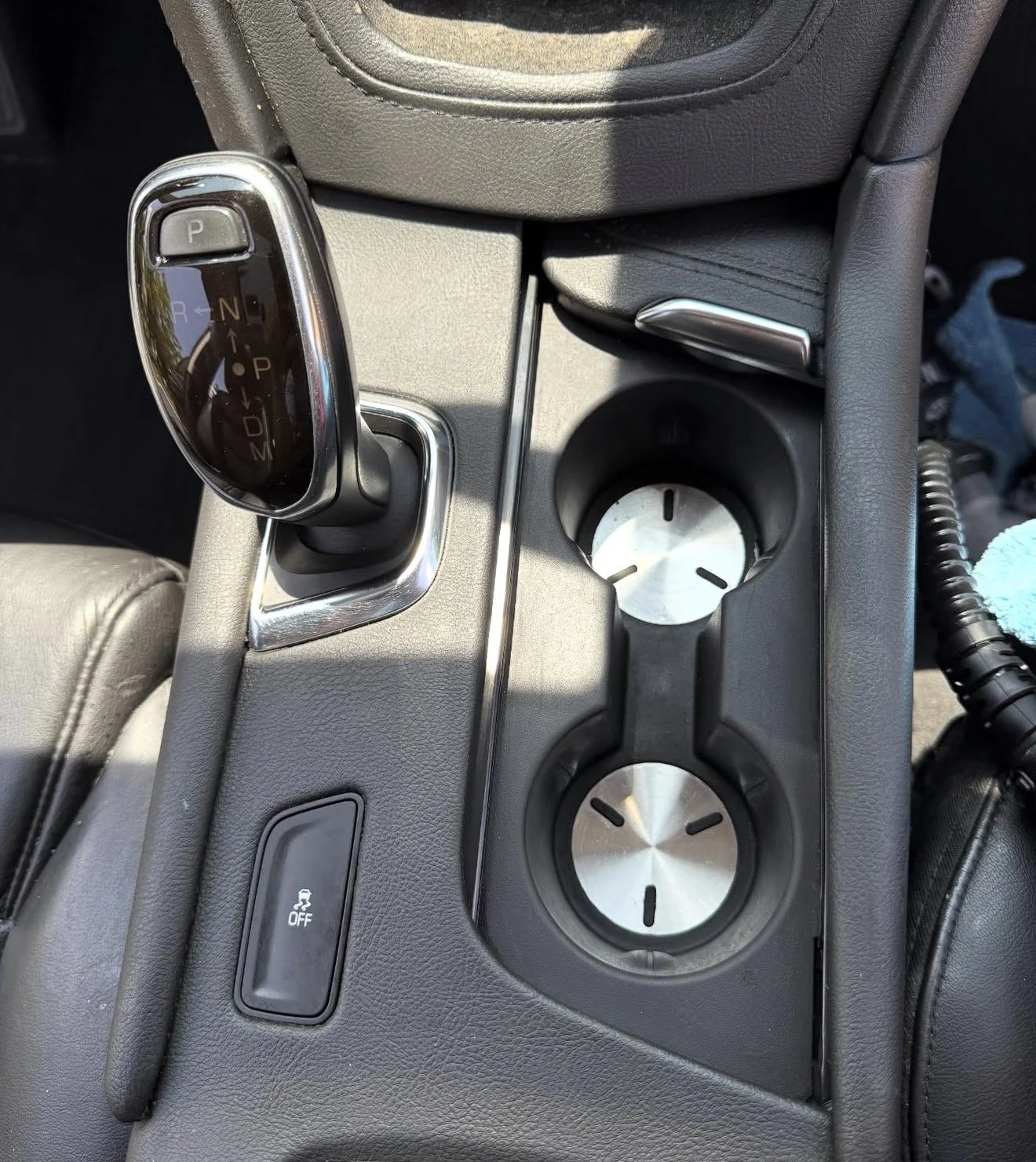 Center console of a car with gear shift, two cup holders, and a button for traction control.