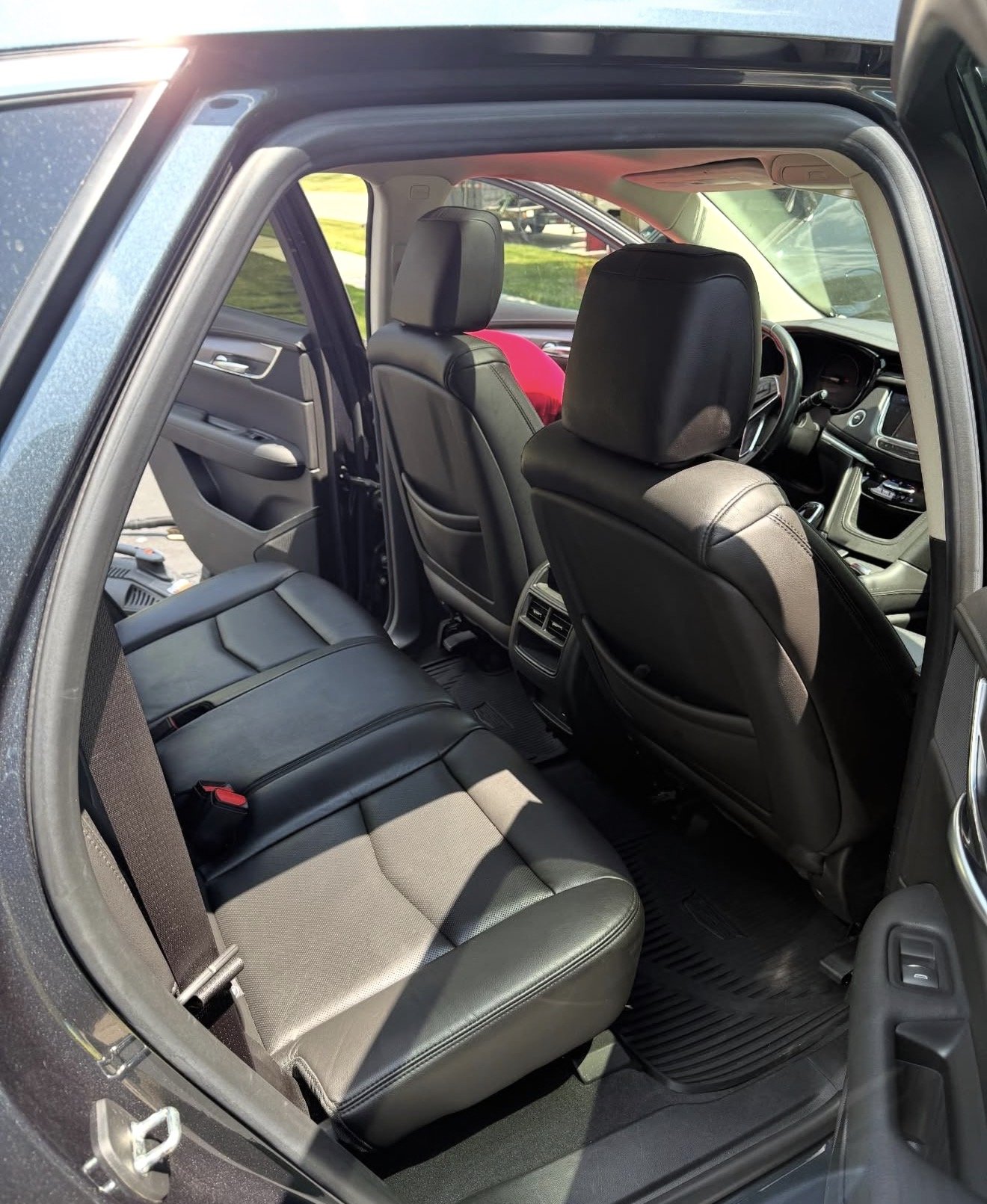 Interior view of a car showing the backseat and front seats with black leather upholstery, dashboard, and windows with a view of greenery outside.