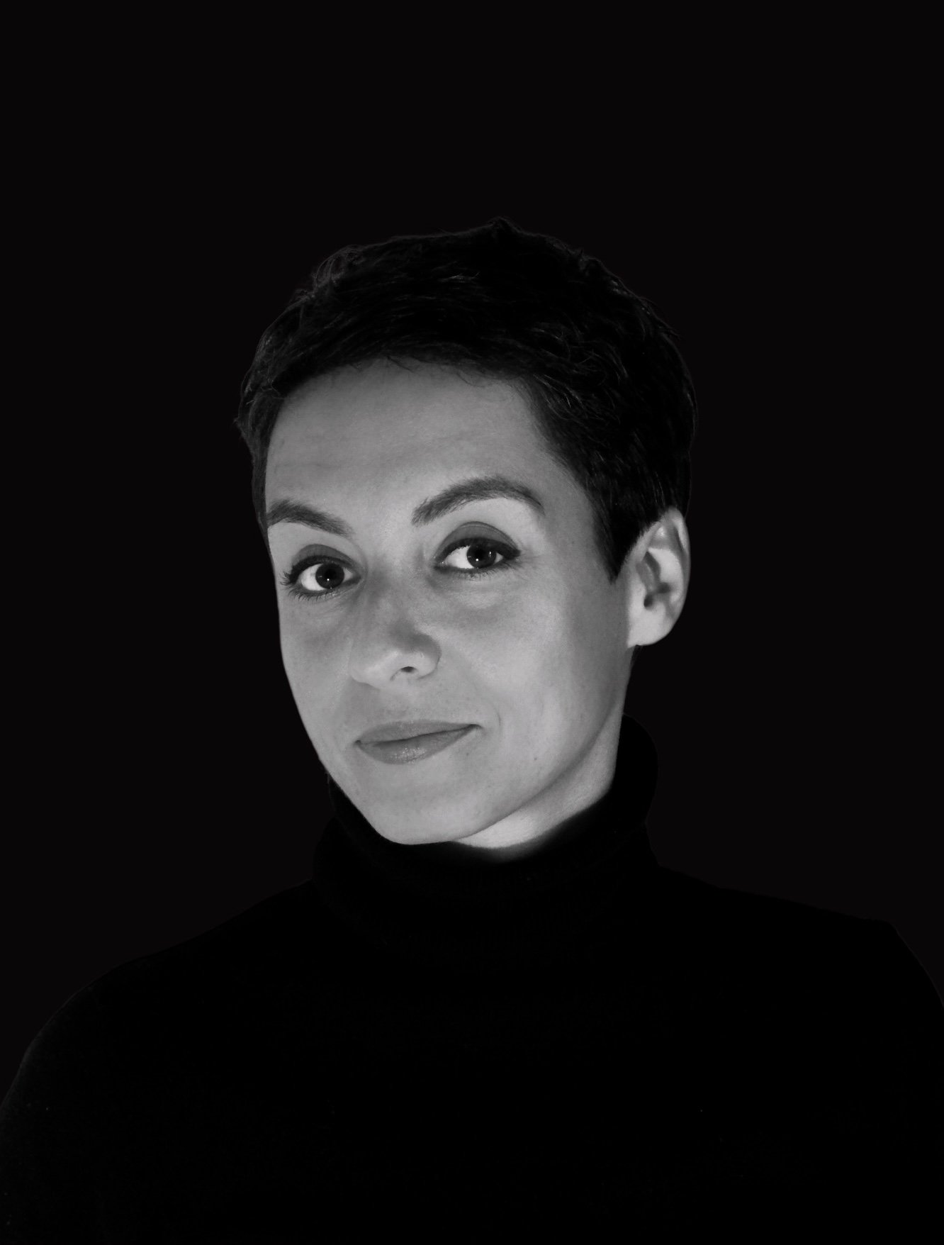 Portrait noir et blanc d'une femme avec des cheveux courts, portant un pull noir, fond noir