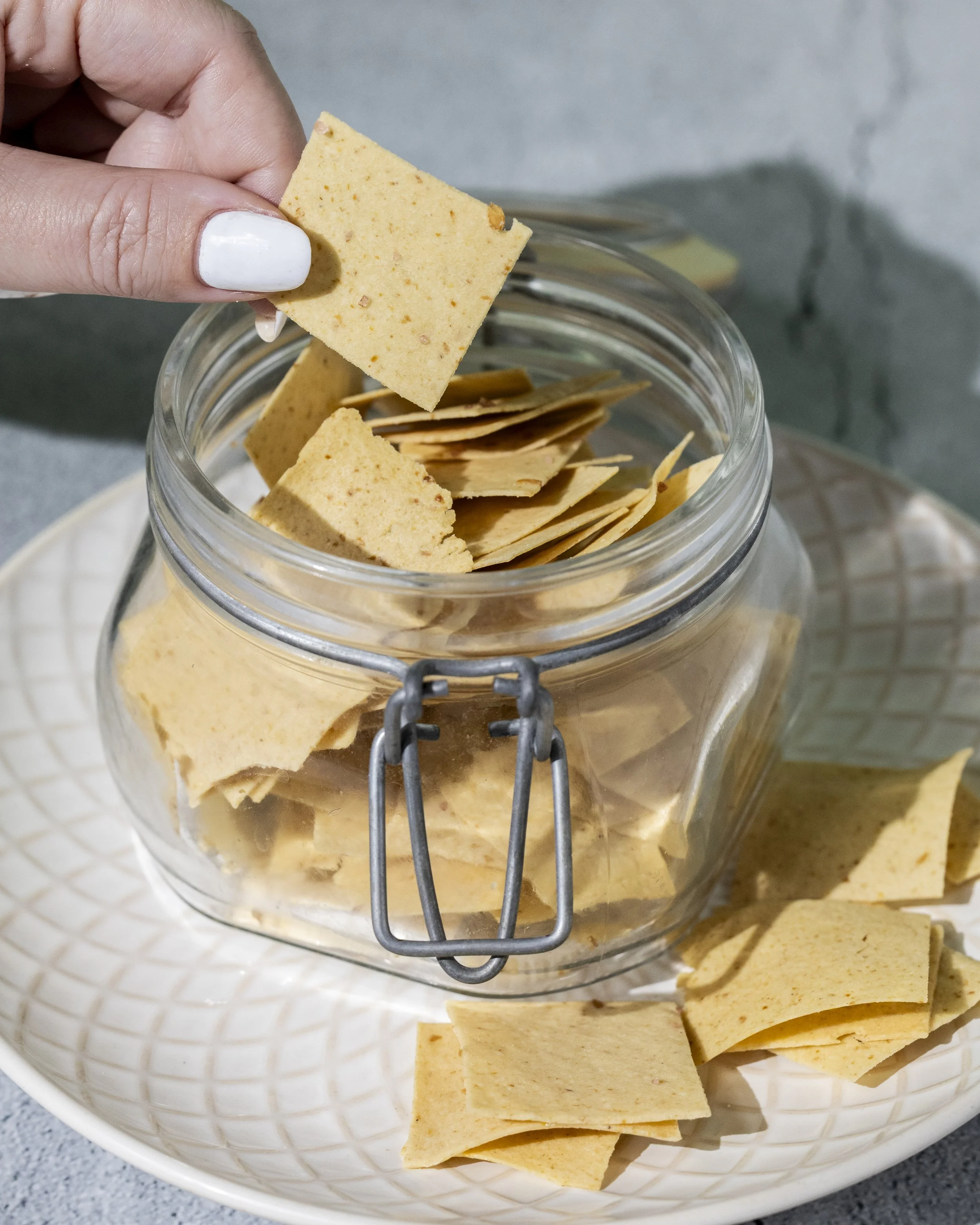 Hand placing a square piece of cheese snack onto a bowl filled with similar cheese snacks.