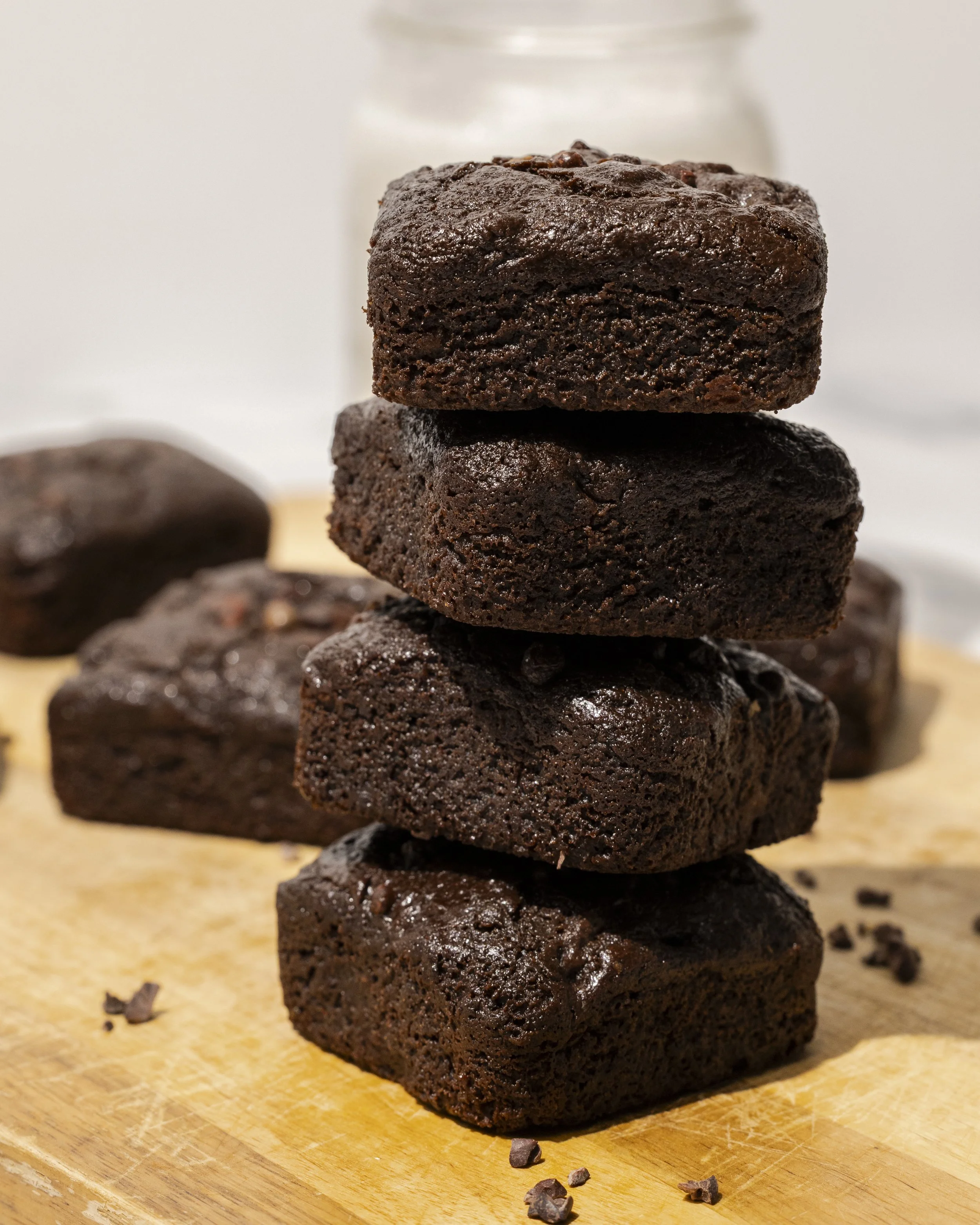 Stacked chocolate brownies on a wooden cutting board with chocolate chunks around.