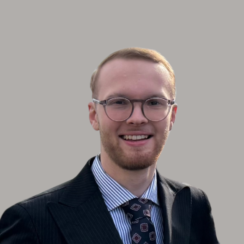 A young man in a business suit smiling at the camera against a plain background.