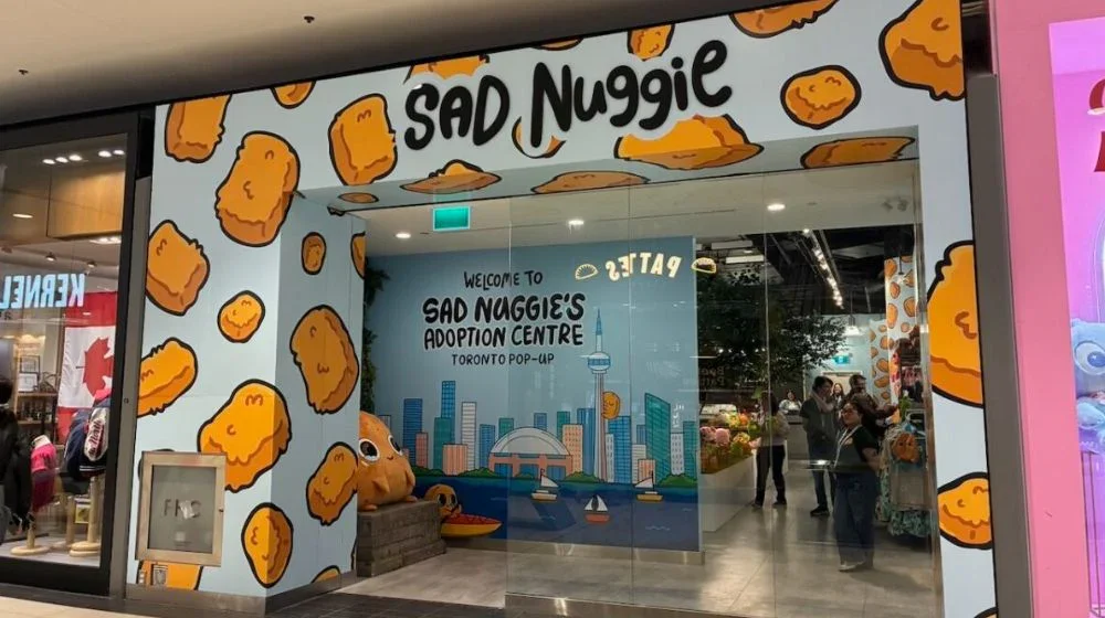 Storefront for 'Sad Nuggie,' a Toronto plushie adoption center, with cheerful chicken nugget graphics on the exterior and a cityscape mural inside.