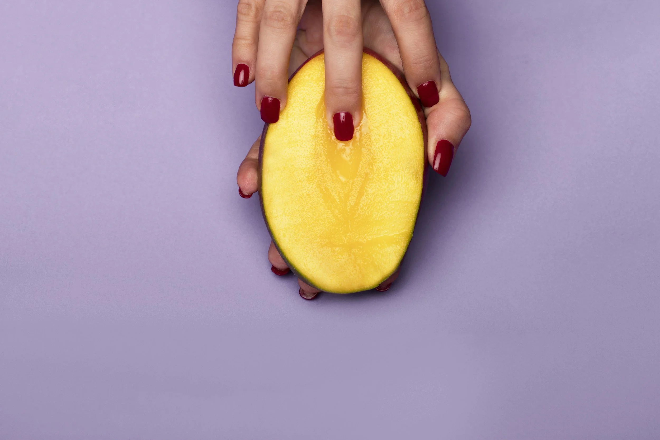 Halved mango with finger touching the center suggestively