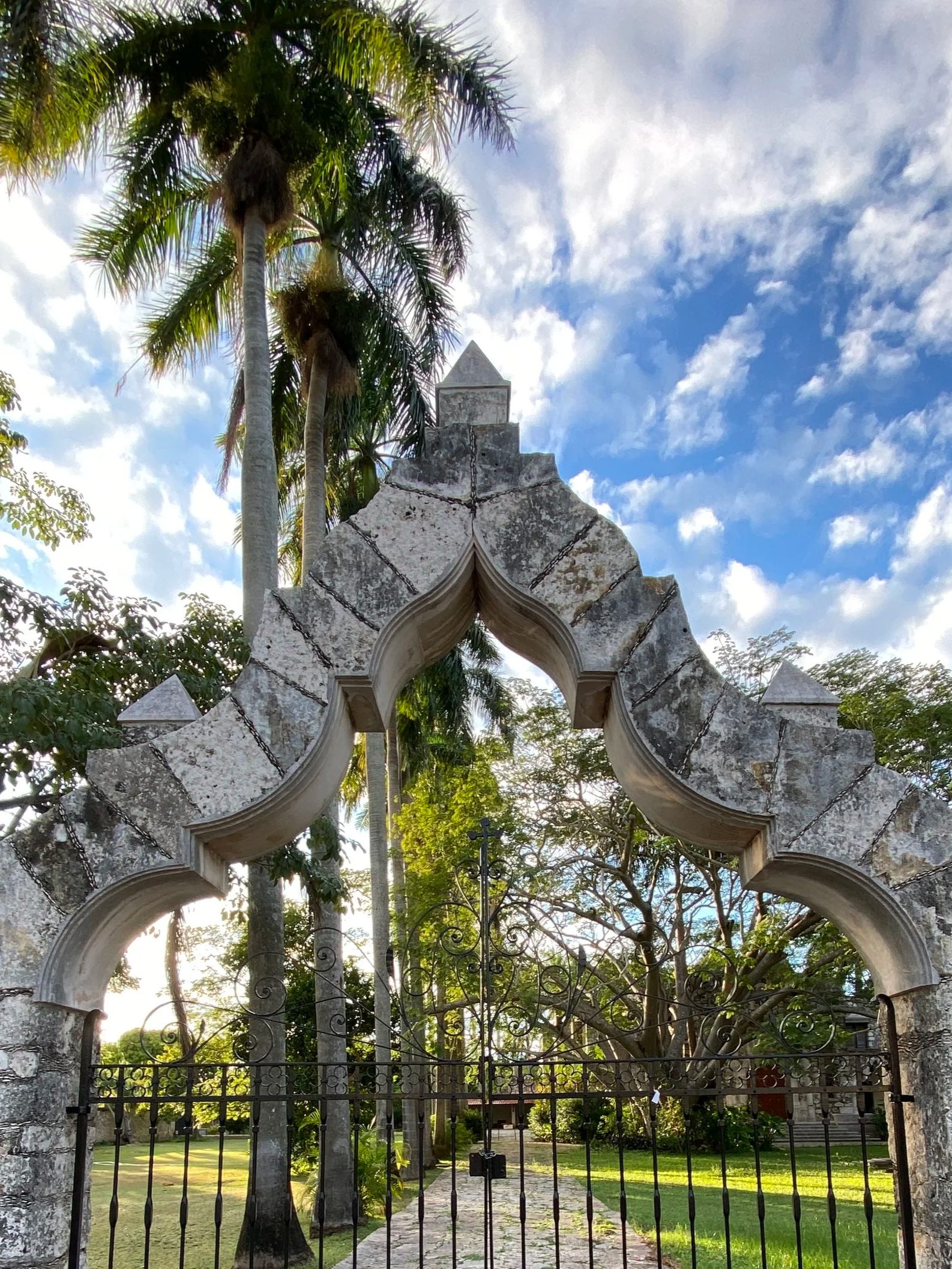 Moroccan style stone and iron gated entrance at Casa Faller with palm trees, vegetation and grass in the background on Av. Perez Ponce in Mérida, Yucatán, Mexico