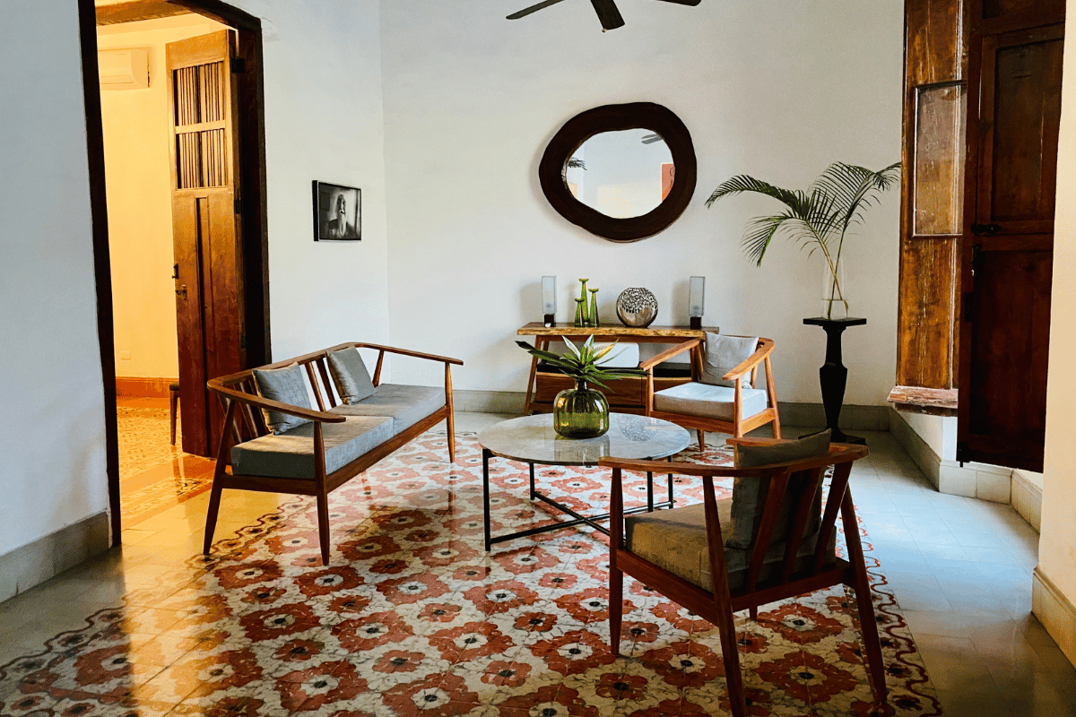 Living room in an Airbnb colonial home featuring red and cream patterned pasta tile flooring, mid-century wooden furniture, and an organic-shaped wall mirror.