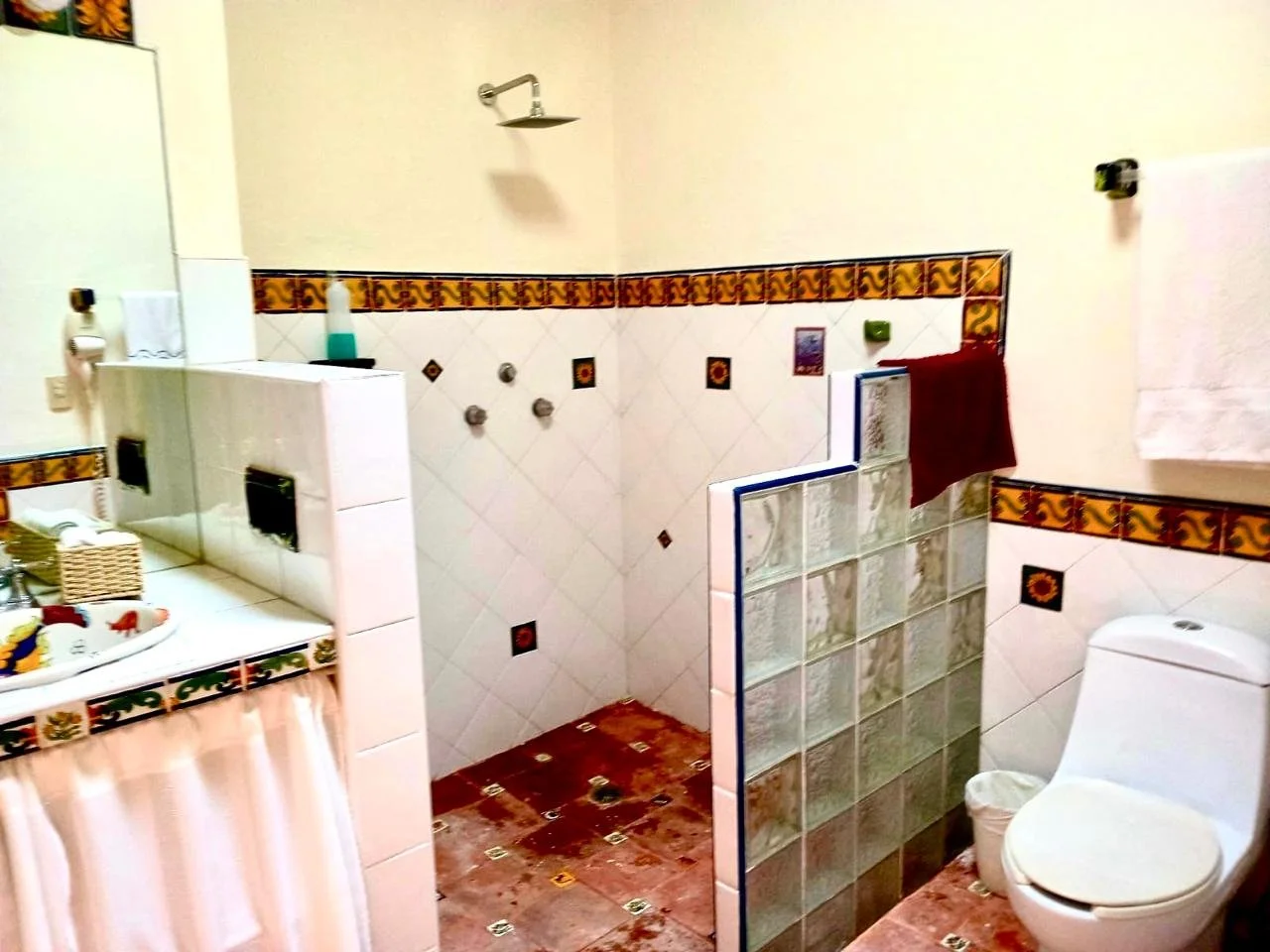 A bathroom with a toilet, a shower area with a partial glass divider, a sink with toiletries, and colorful tile decorations on the walls and floor.