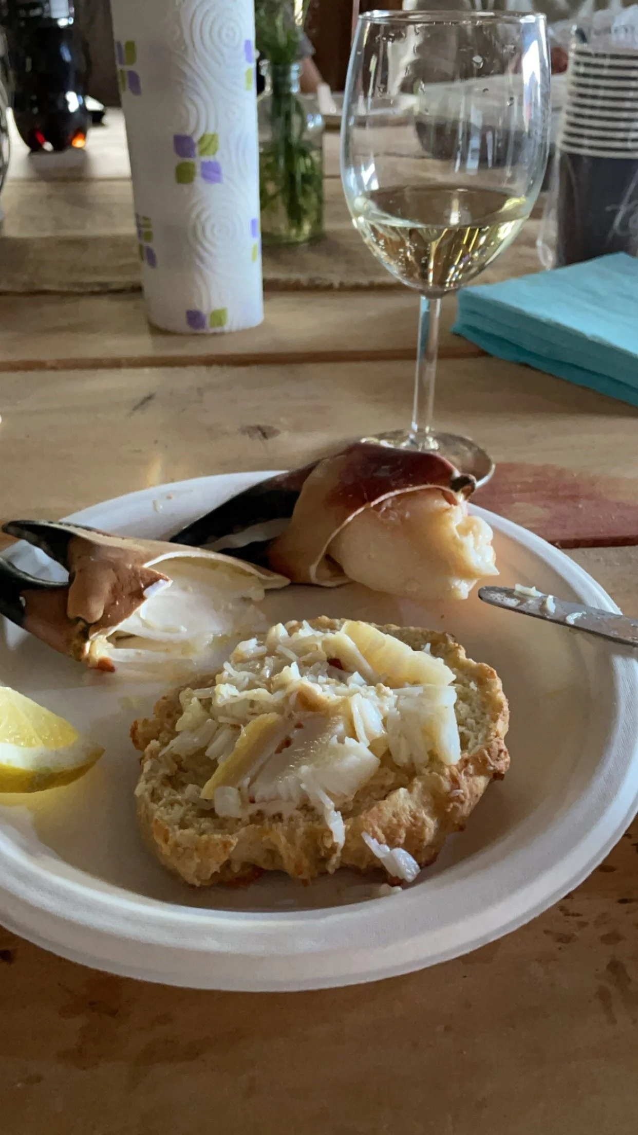 Et fat med ostebrød, reker på en brødskive, sitronbiter, hvitvin i glass, papirservietter og en vannkrukke på et trebord.