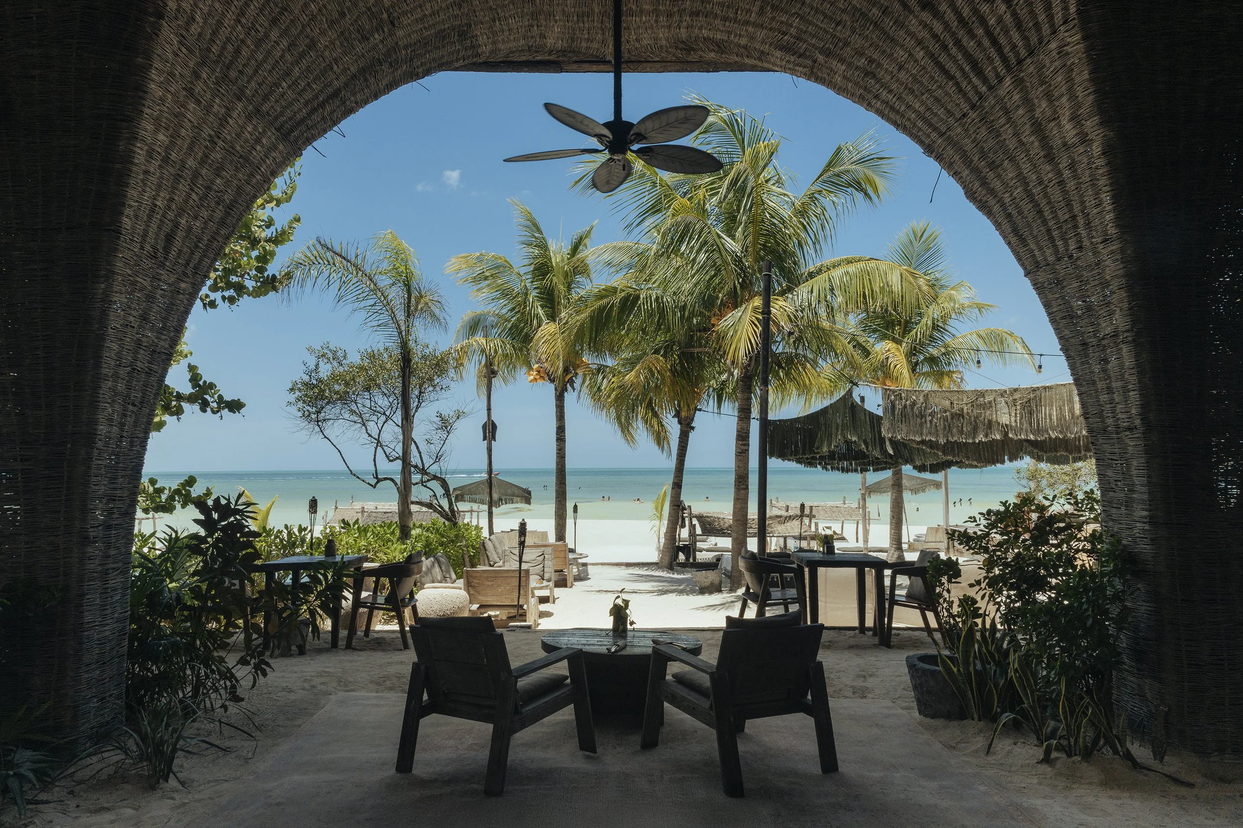 Arco arquitectónico enmarcando playa tropical con palmeras. Hospitalidad de lujo en Holbox.
