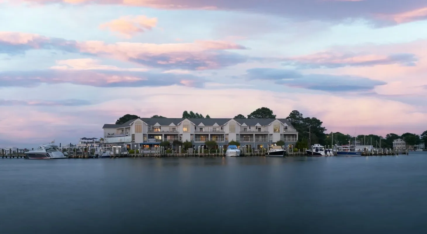 A waterfront residential complex with multiple boats docked along the pier, under a pastel-colored sky at dusk.