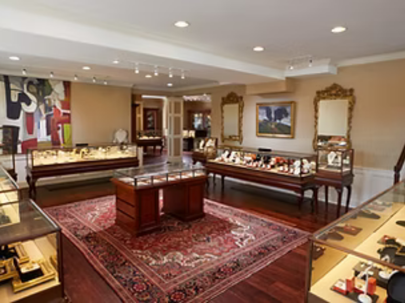 Interior of a jewelry store with display cases, framed artwork, mirrors, and a decorative rug.