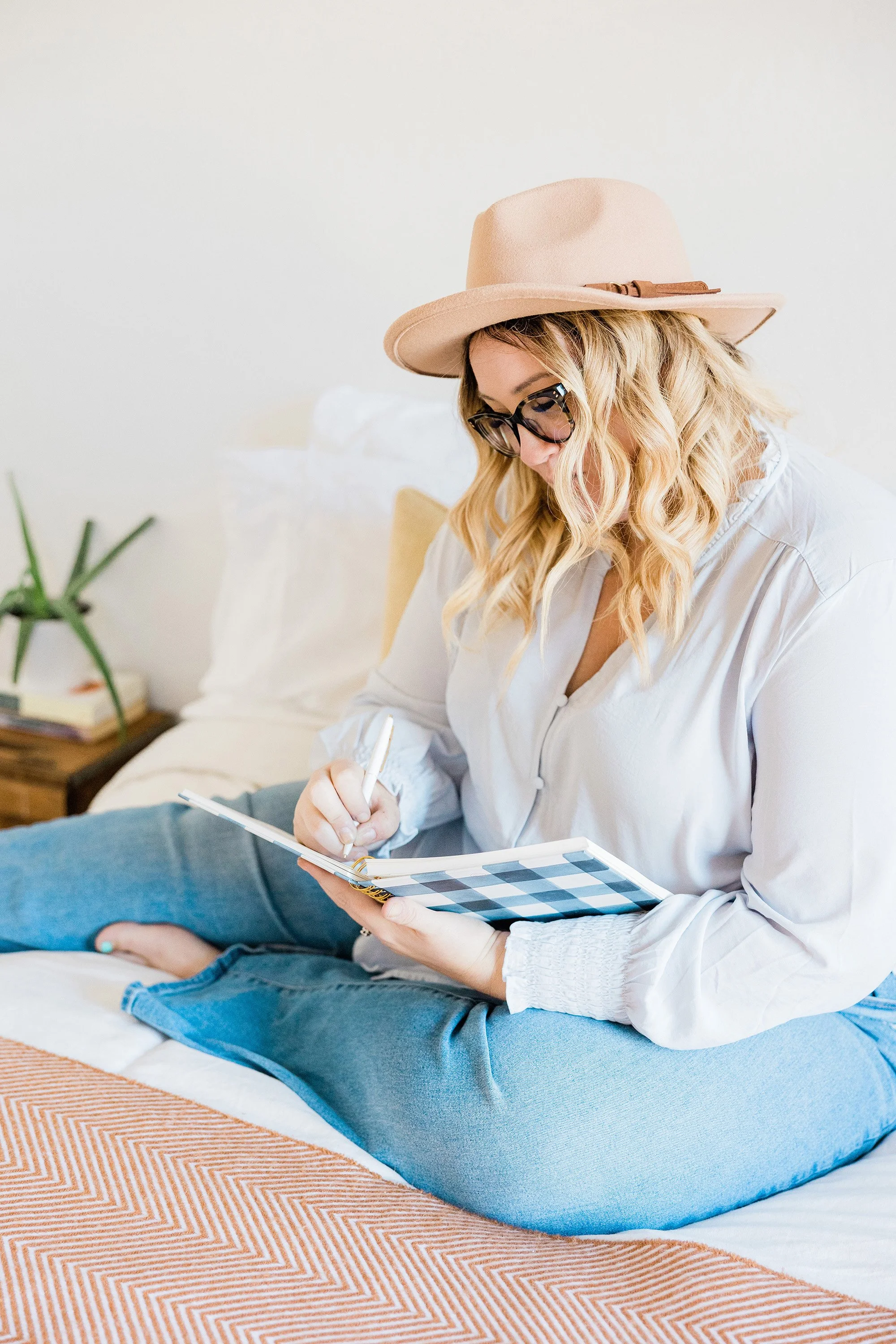 A female small business owner sits on a comfortable chair in a brightly lit room. Her legs are crossed and her is holding a notebook in one hand, pen in the other.