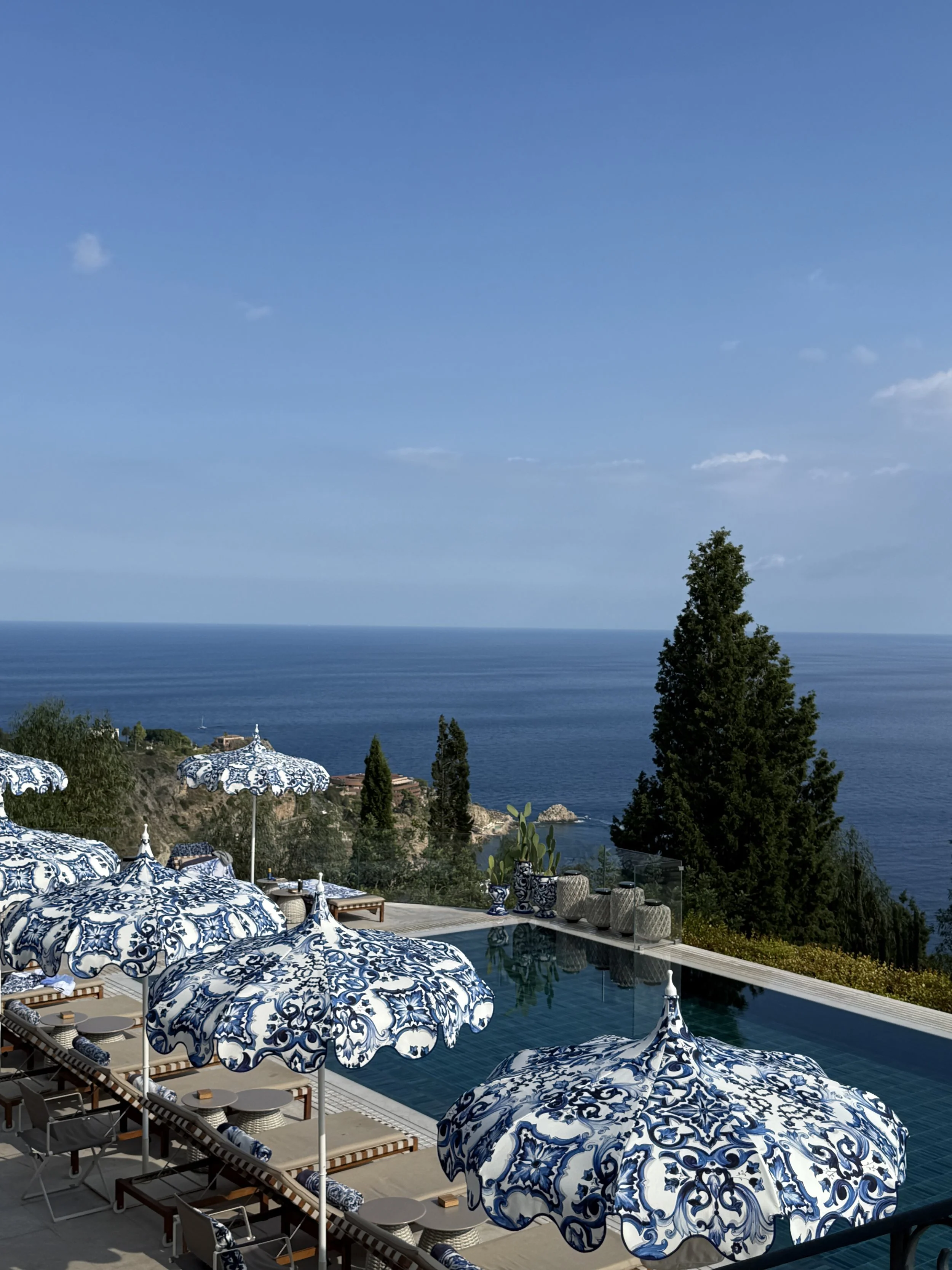 Luxury outdoor pool area with blue and white patterned umbrellas and lounge chairs overlooking the ocean horizon.