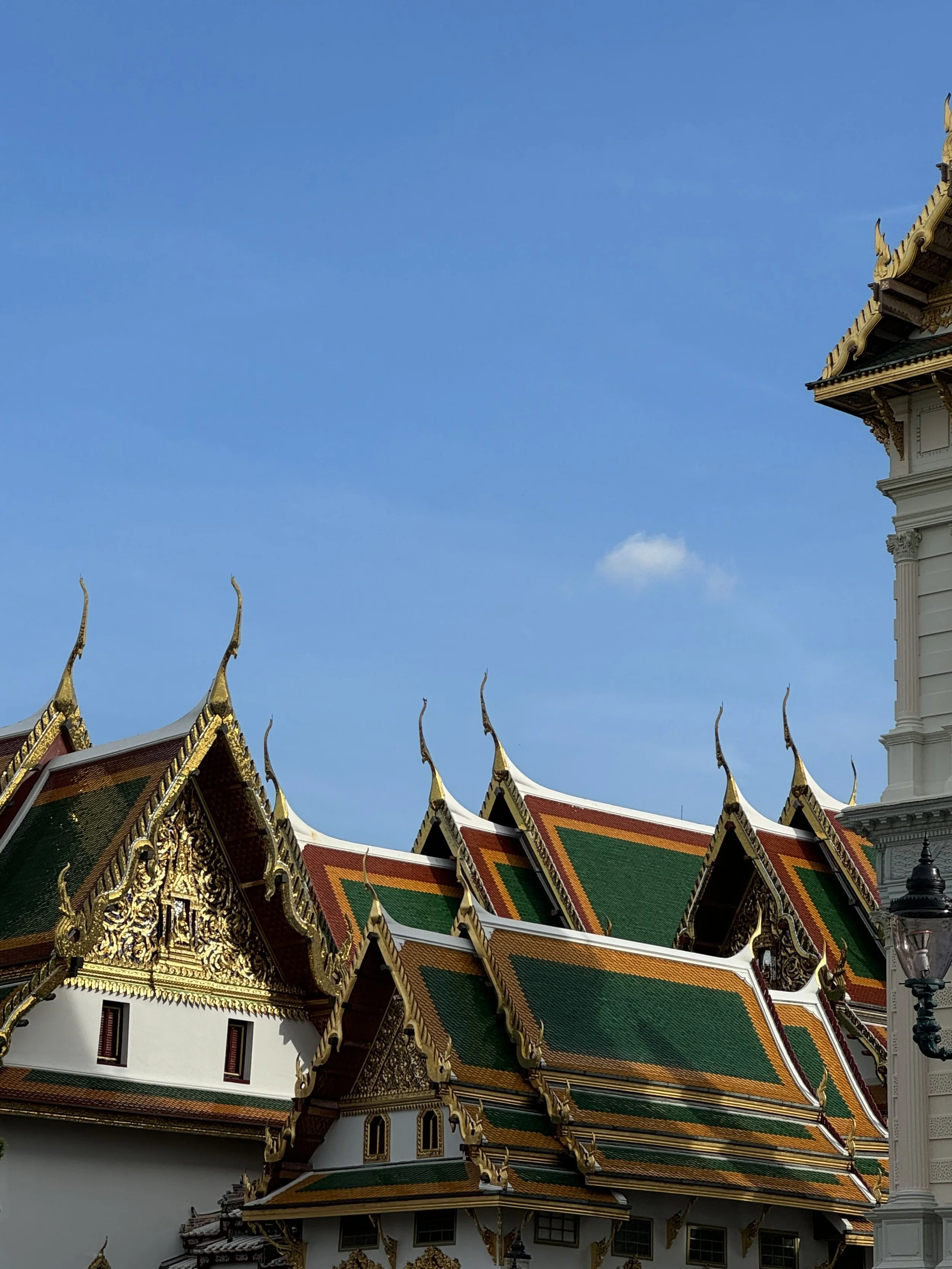 Traditional Thai temple with ornate, multi-tiered roof decorated with gold and green tiles, set against a blue sky.