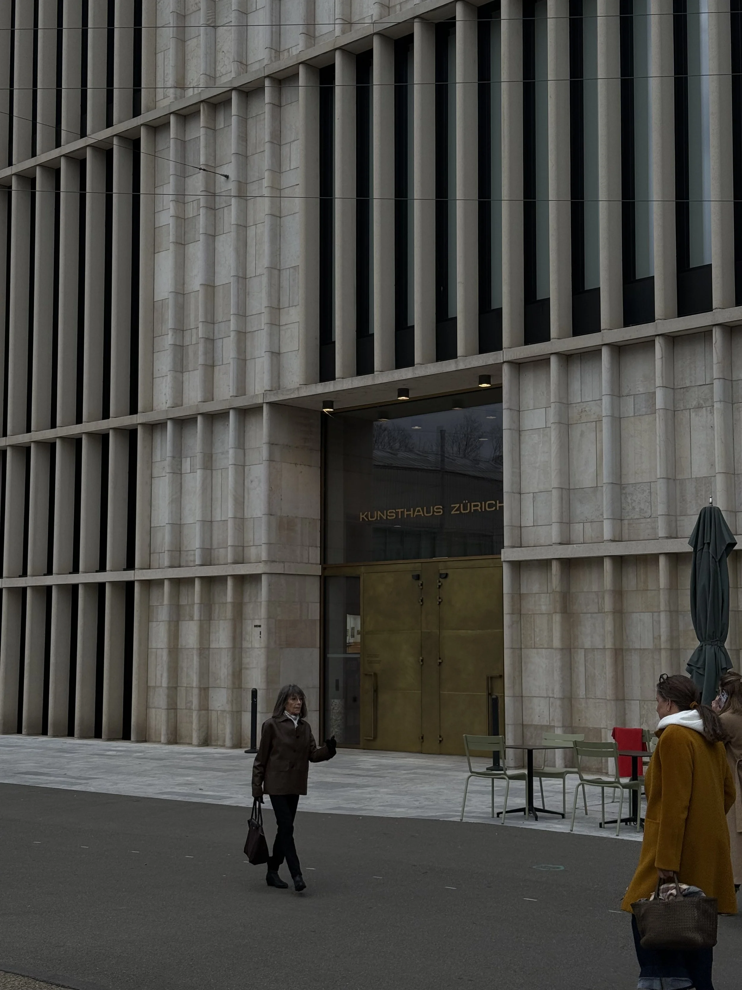 People walking in front of a modern building with large glass windows and vertical concrete columns, with the entrance labeled 'KUNSTHAUS ZURICH'.