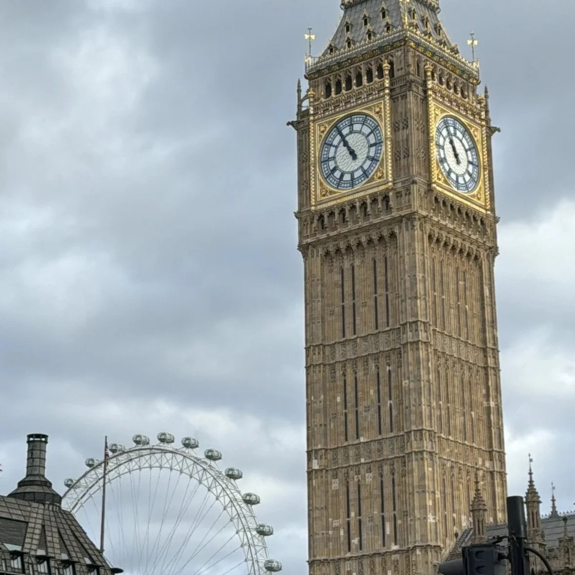 Big Ben clock tower in London with a London Eye Ferris wheel in the background, cloudy sky.