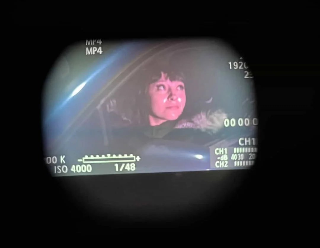 A woman looking up through a camera viewfinder, with camera settings and information visible on the screen.