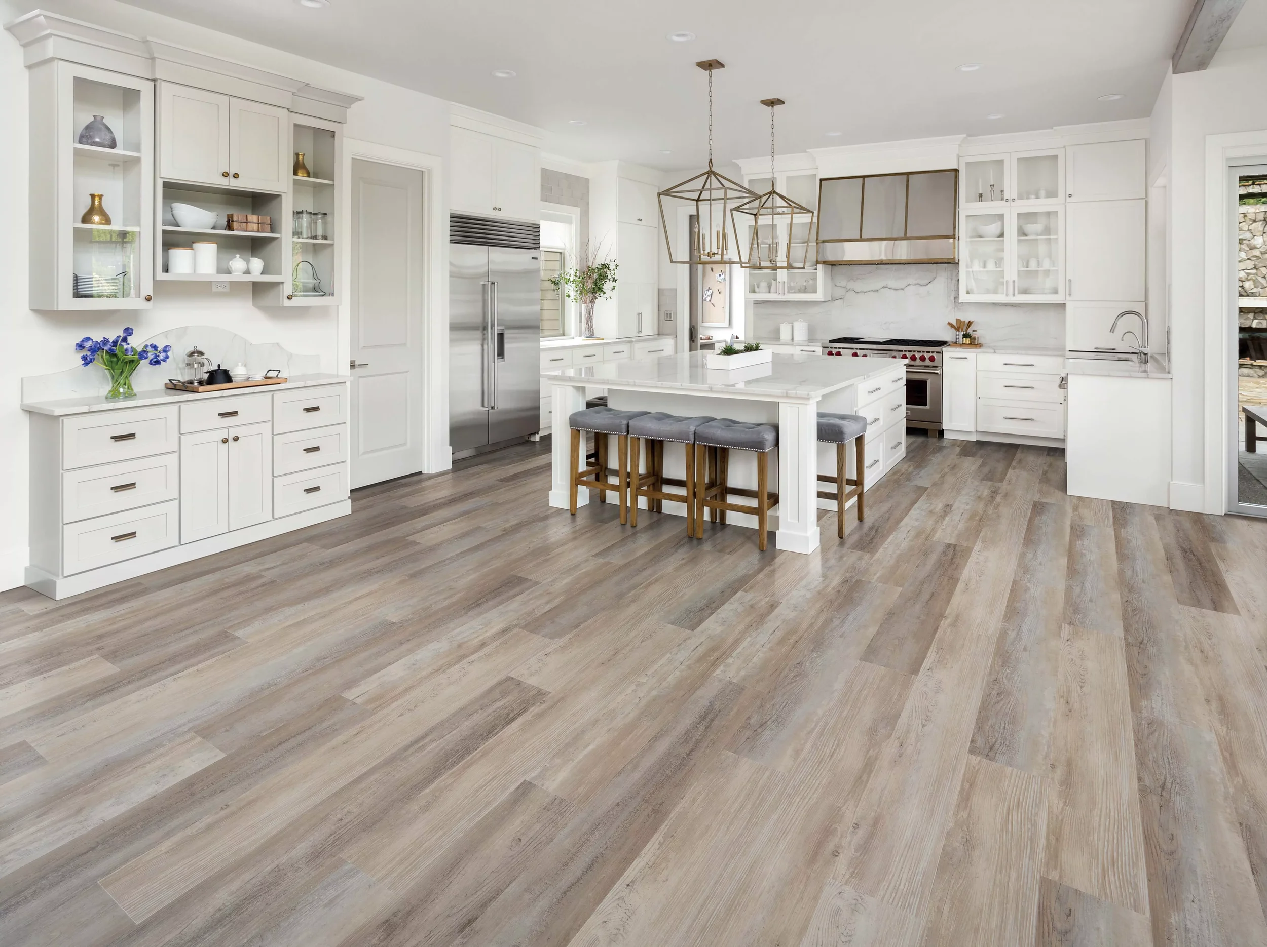 Modern white kitchen with marble countertops, wooden flooring, and gold-accented lighting fixtures.