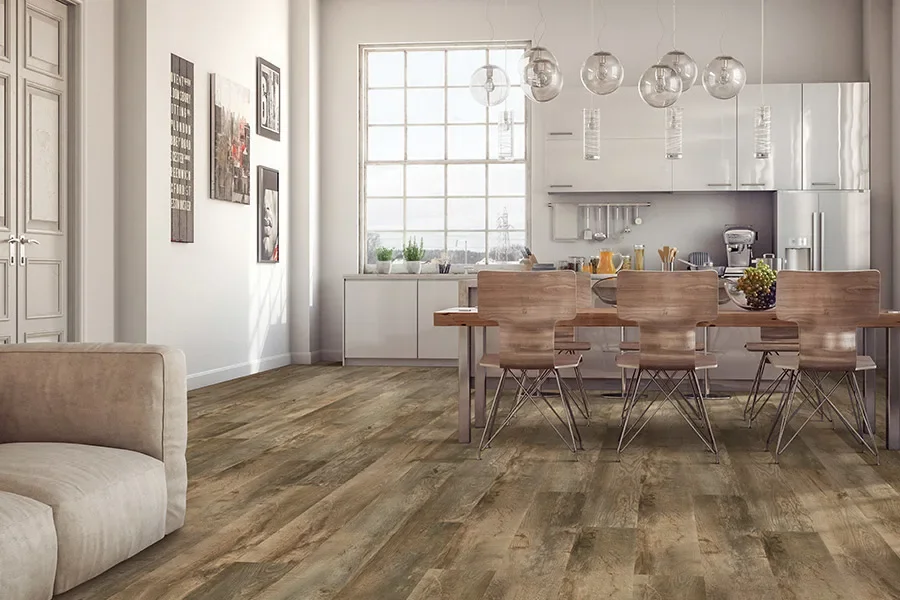 Modern open-concept kitchen and dining area with wooden floor, white cabinetry, and a wooden dining table with six chairs, illuminated by hanging glass pendant lights.
