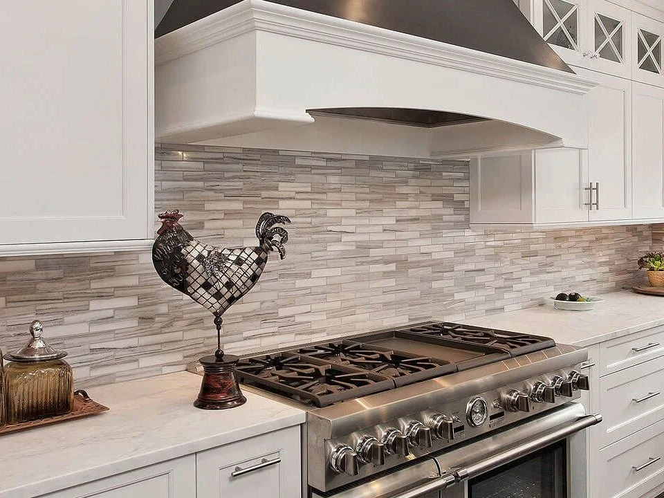 Kitchen with white cabinets and a stainless steel stove, decorative rooster sculpture on the counter, small bowl and basket of vegetables, tile backsplash.