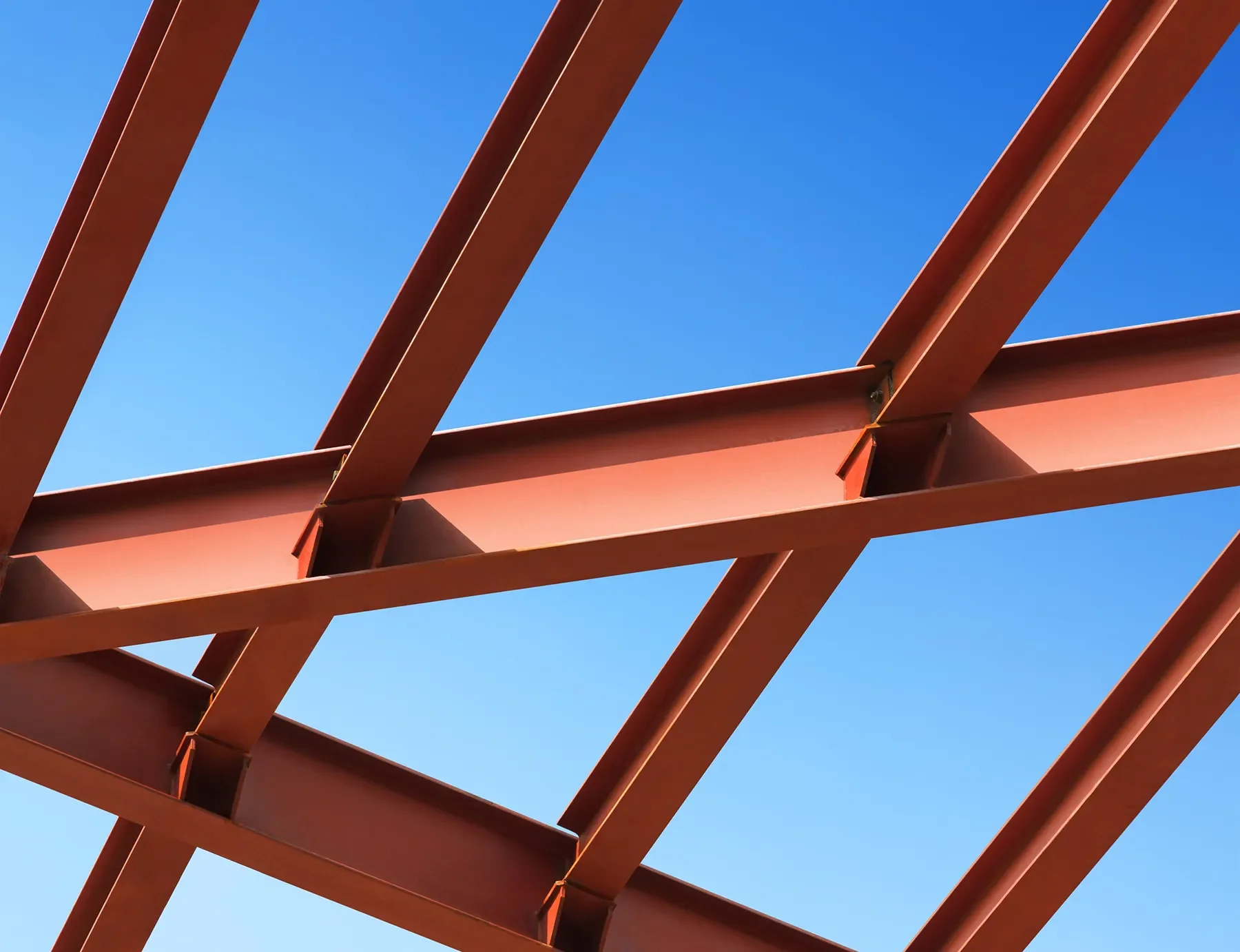 Close-up of a rust-colored steel framework against a clear blue sky, showing intersecting beams and structural supports.