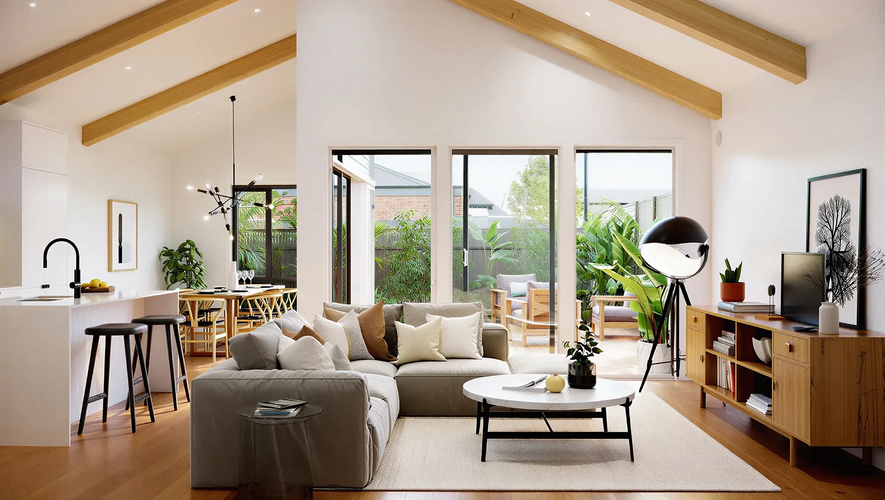 Bright living room with white sofa, beige pillows, round coffee table, large windows, outdoor patio with greenery, wooden ceiling beams, TV on wooden media console, decorative plants.