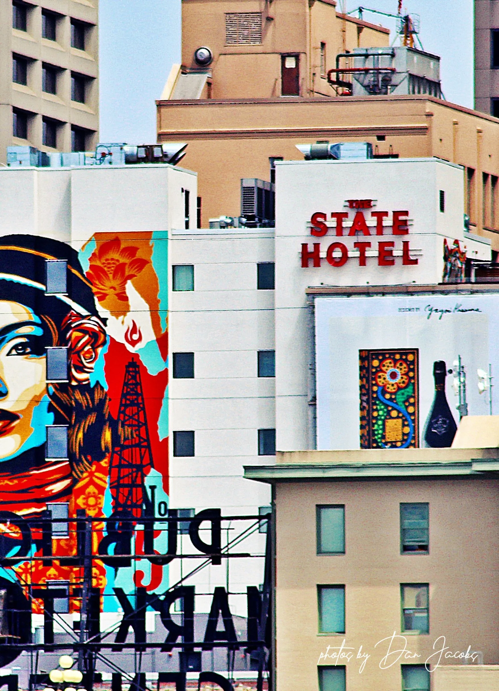 Multi-story urban buildings with colorful murals and a red sign that reads 'The State Hotel'.