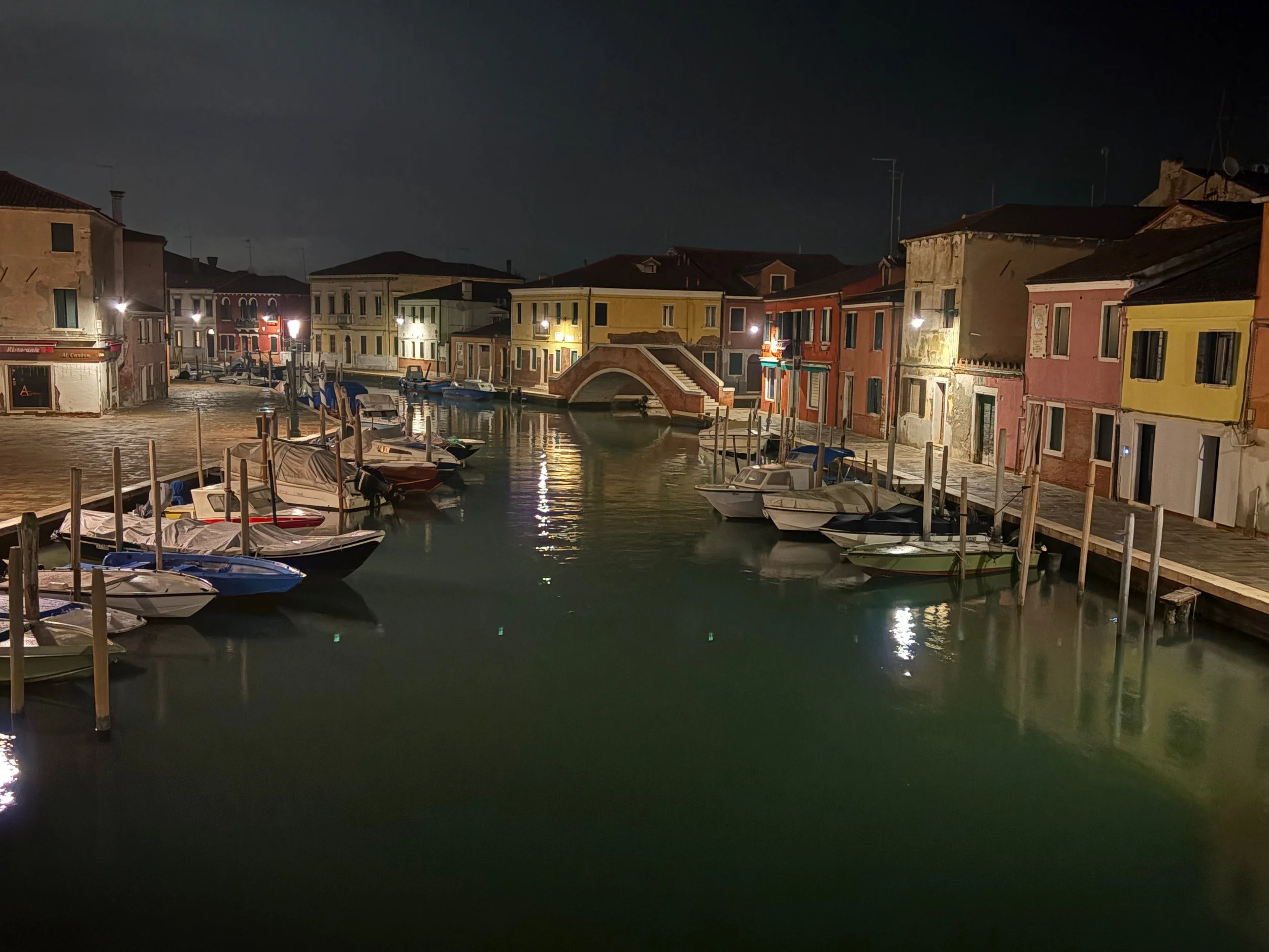 Nighttime view of a canal lined with colorful buildings and boats, illuminated by streetlights.