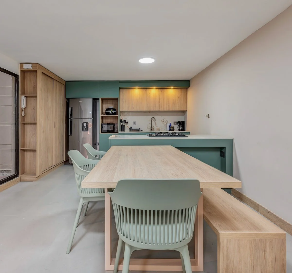 Cocina moderna con mesa de madera y sillas color verde, armarios de madera y electrodomésticos de acero inoxidable.