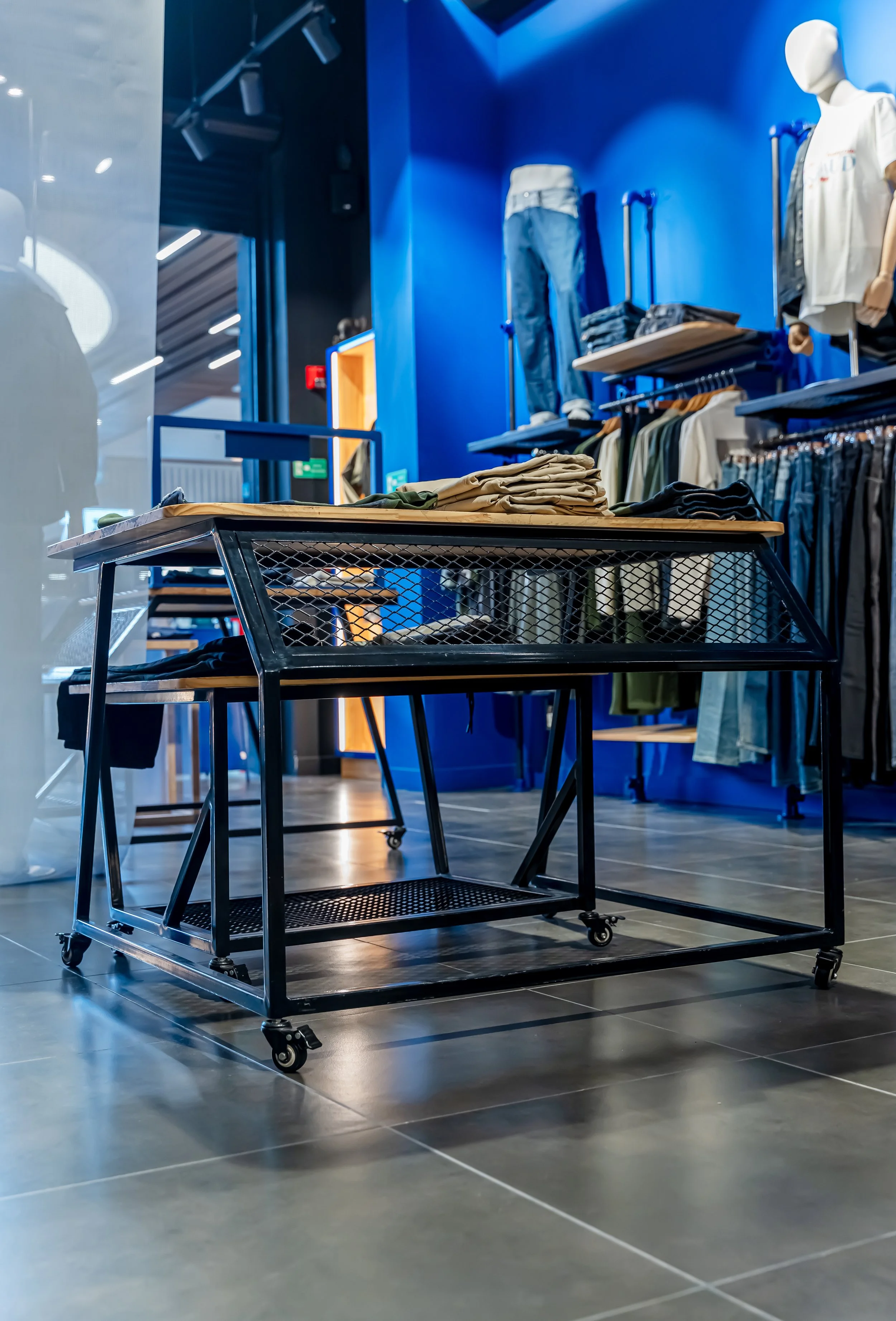 Tienda de ropa con varias prendas en exhibición y una mesa de metal con ruedas en primer plano.
