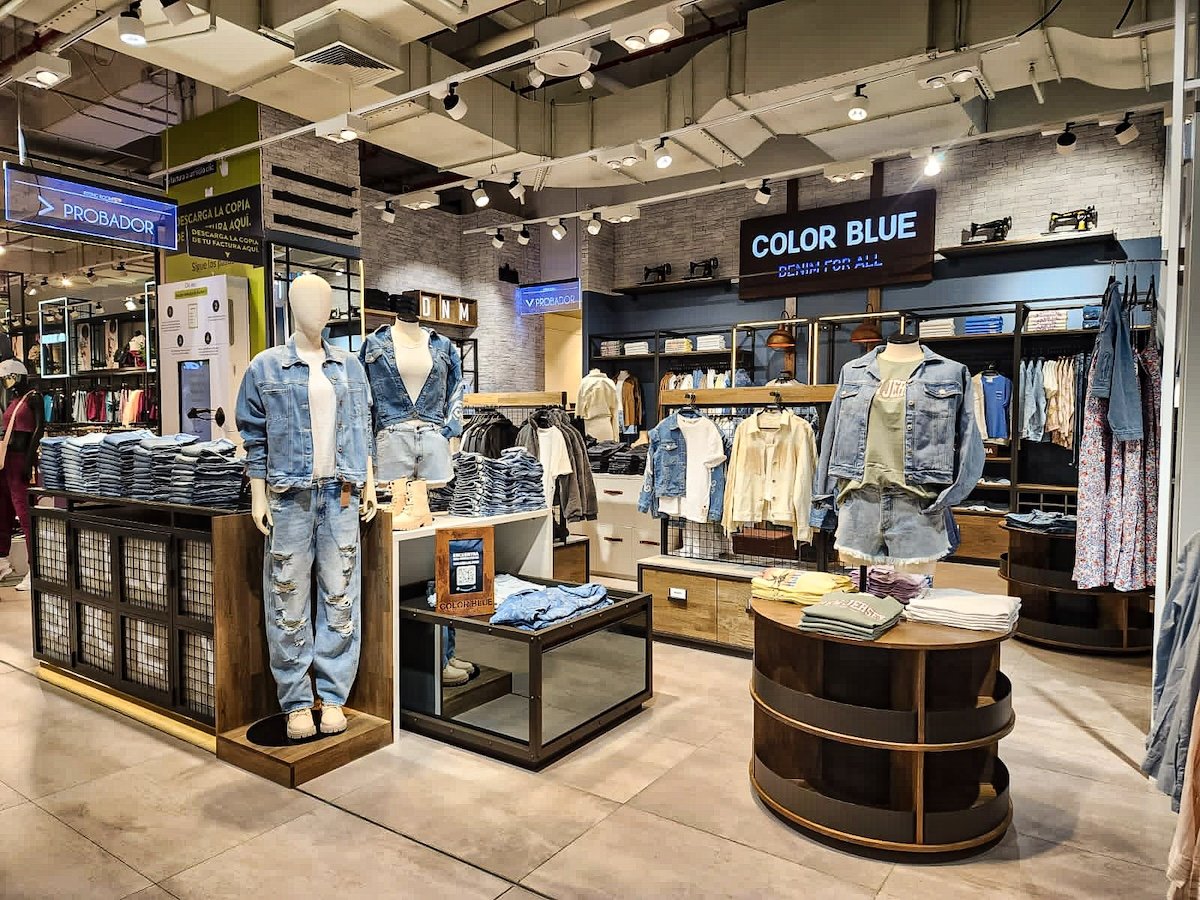 Sección de ropa de mezclilla en una tienda, con maniquíes vestidos con chaquetas y jeans, y estantes con prendas dobladas.