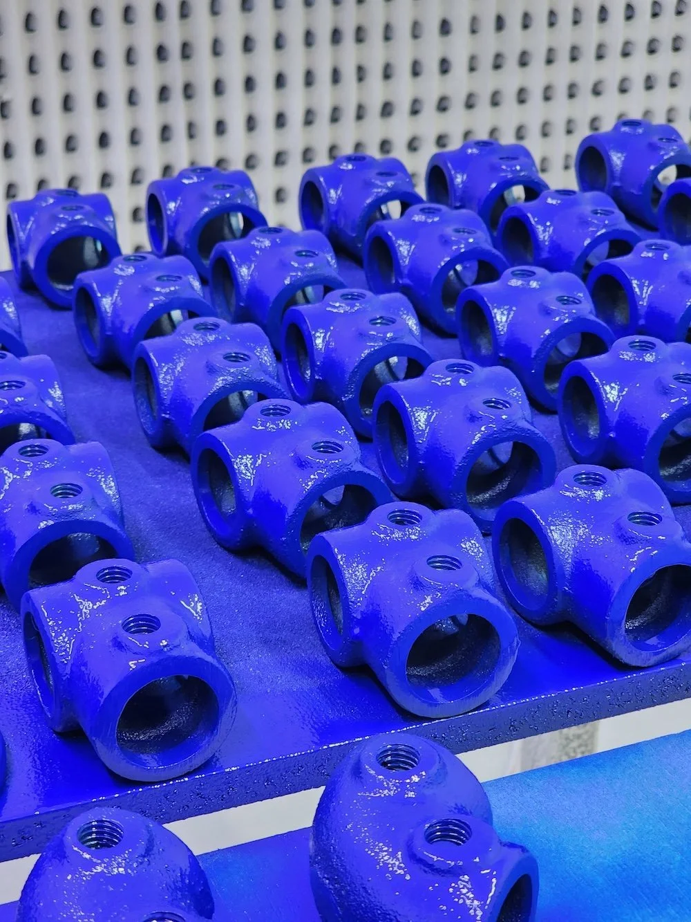 Varios componentes metálicos pintados de azul organizados en filas en una mesa de trabajo.
