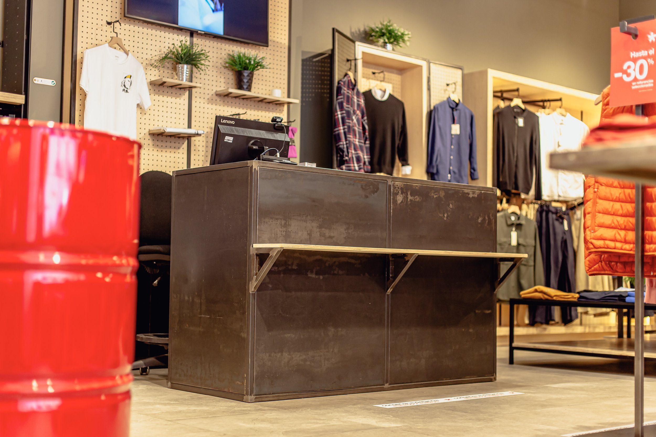 Interior de una tienda de ropa con prendas en perchas y una señal de hasta 30% de descuento.