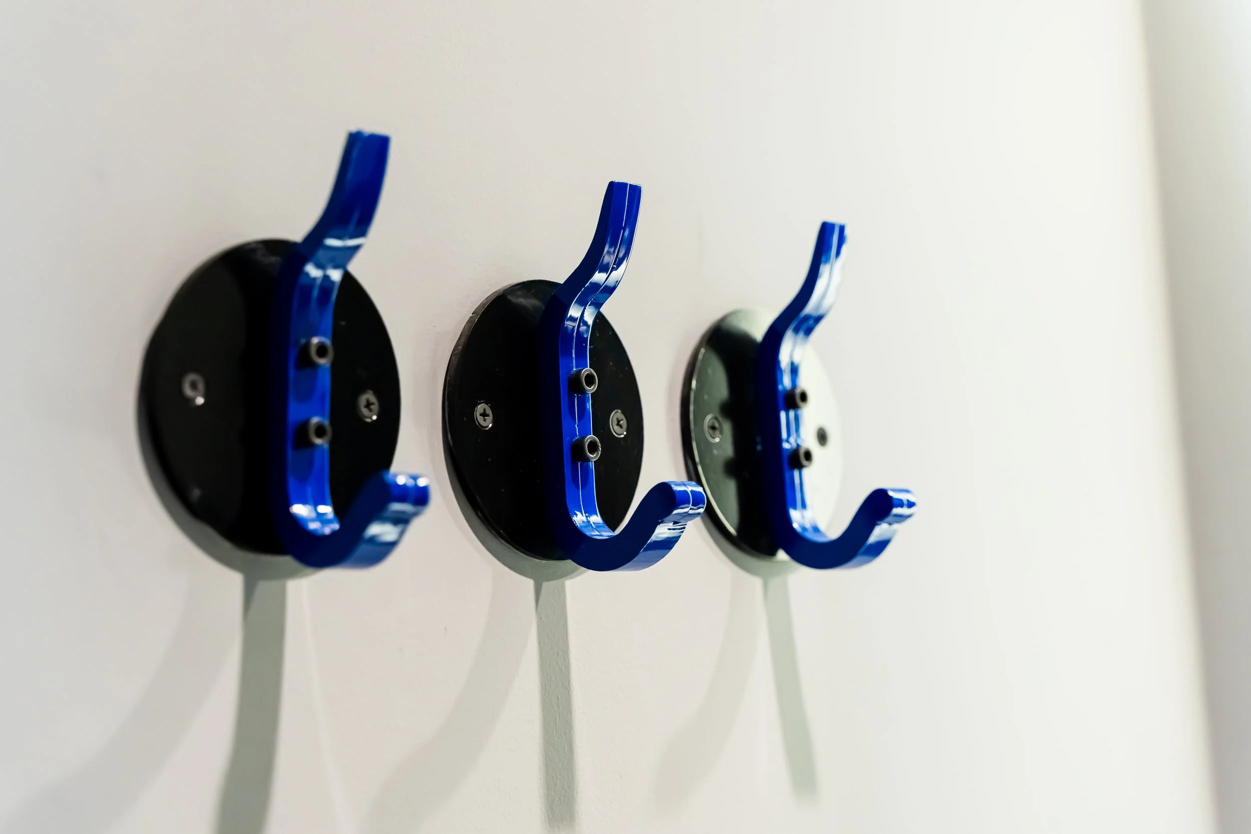 Tres ganchos de madera pintados de azul, montados en una pared blanca, formando una fila horizontal.