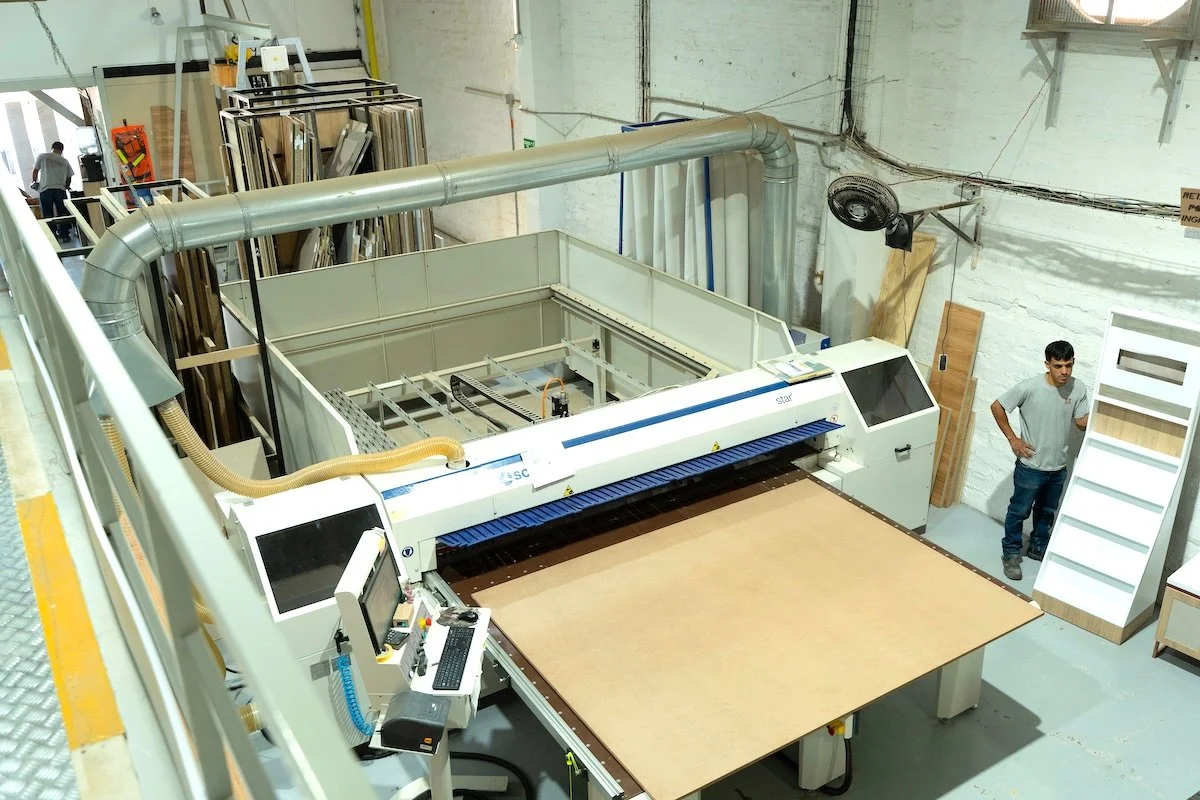 Maquina láser de corte y grabado en un taller de carpintería, con un operario de pie observando.