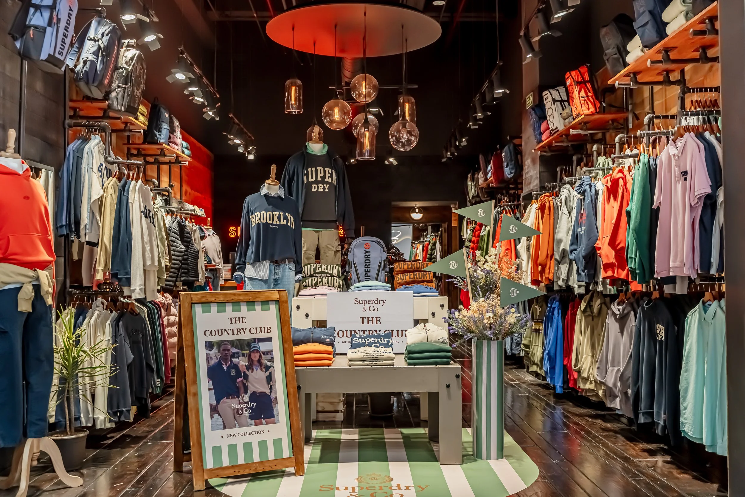 Interior de una tienda de ropa con exhibiciones de prendas deportivas y accesorios, decorada con iluminación moderna y adornos en tonos cálidos.
