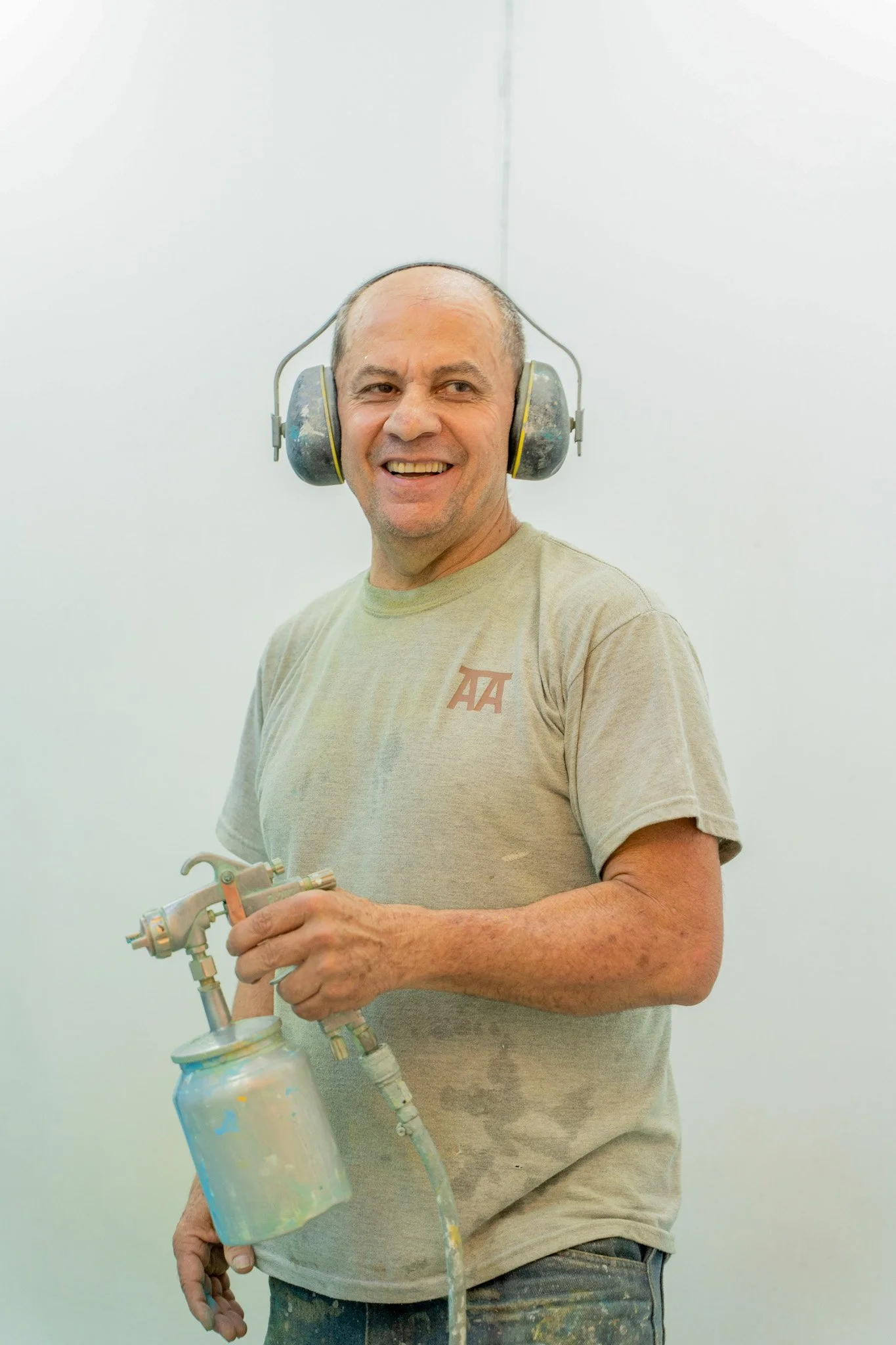 Hombre sonriendo, usando protección auditiva, sosteniendo un equipo de pintura en aerosol.