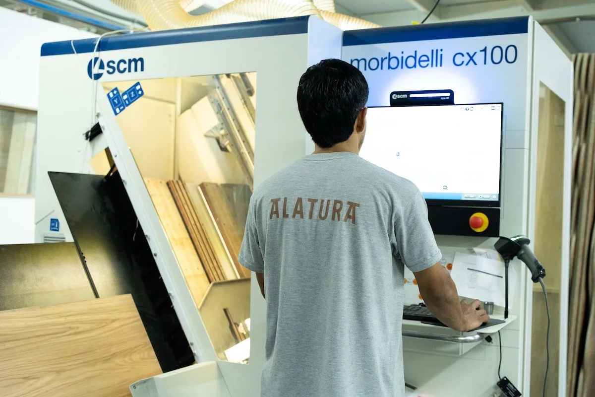 Un operario utilizando una máquina CNC en un taller de carpintería, con un monitor y un control digital.
