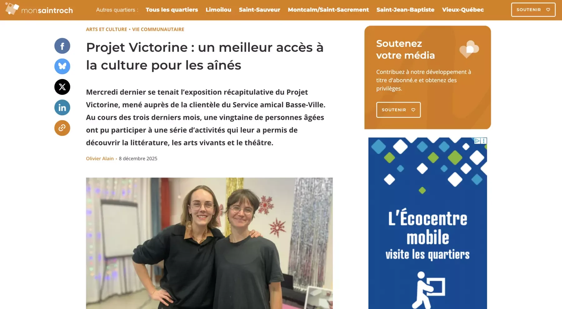 Deux femmes souriantes posent ensemble dans une salle décorée avec des guirlandes lumineuses et des décorations de Noël, un sapin visible à l'arrière.