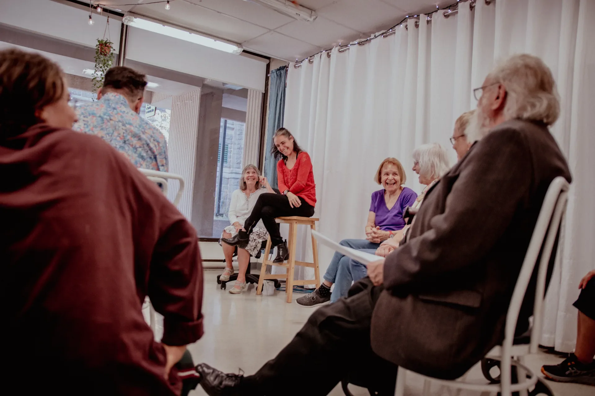 Groupe de personnes assises en cercle lors d'une activité ou d'une discussion, avec une femme en rouge qui sourit et parle.