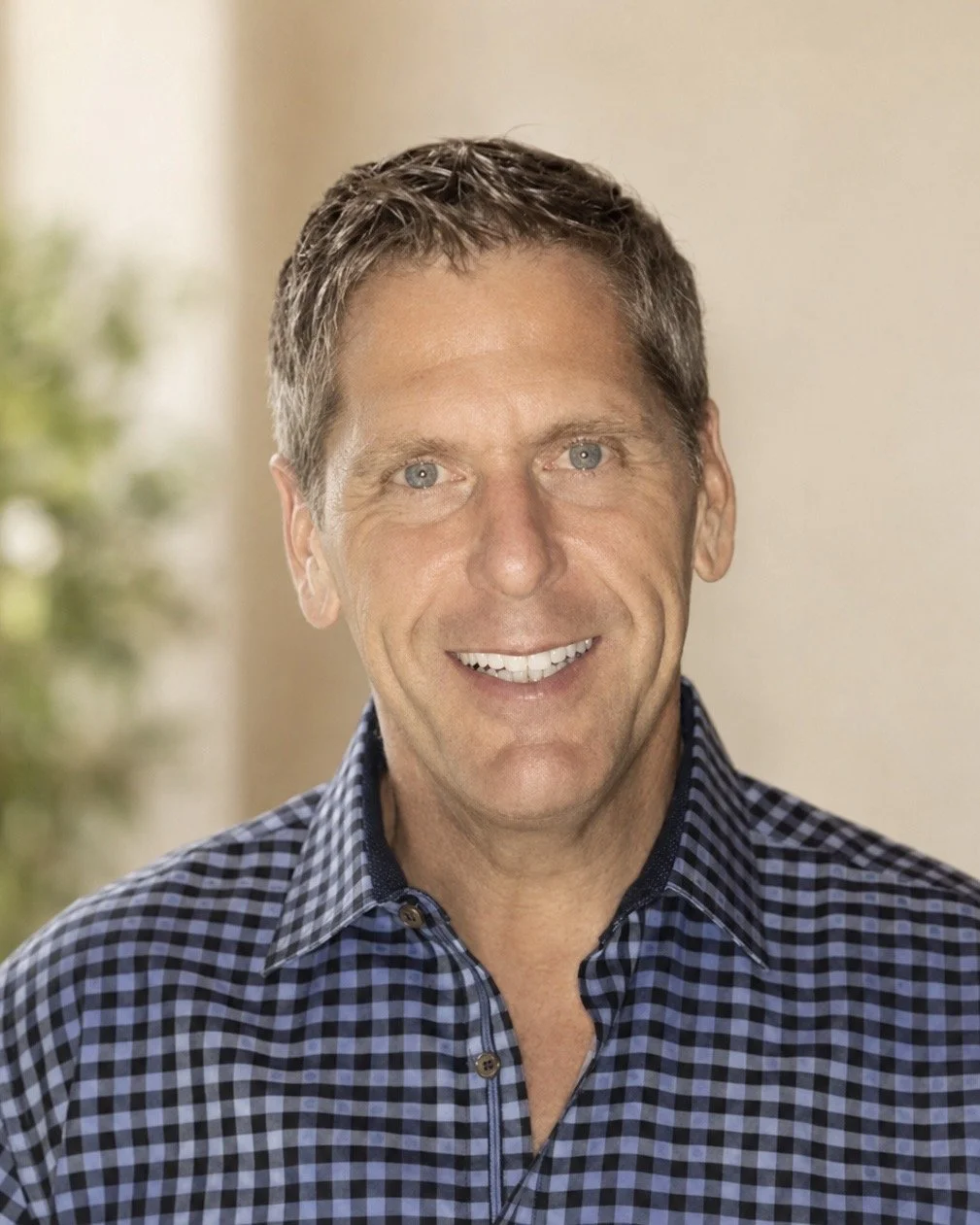 Headshot of a smiling middle-aged man with short brown hair wearing a blue and black checkered shirt.