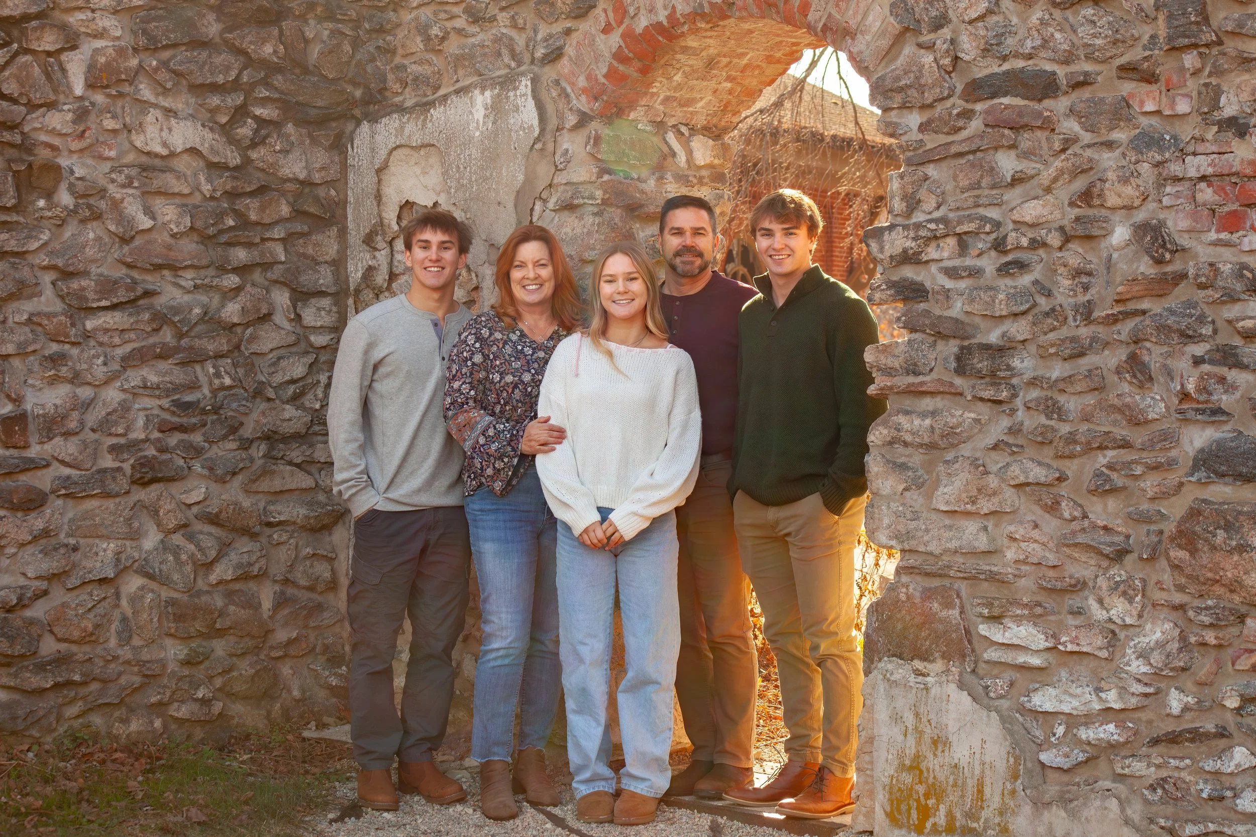 Family of five smiling together at golden hour in a rustic stone archway, Chester County PA family portrait session