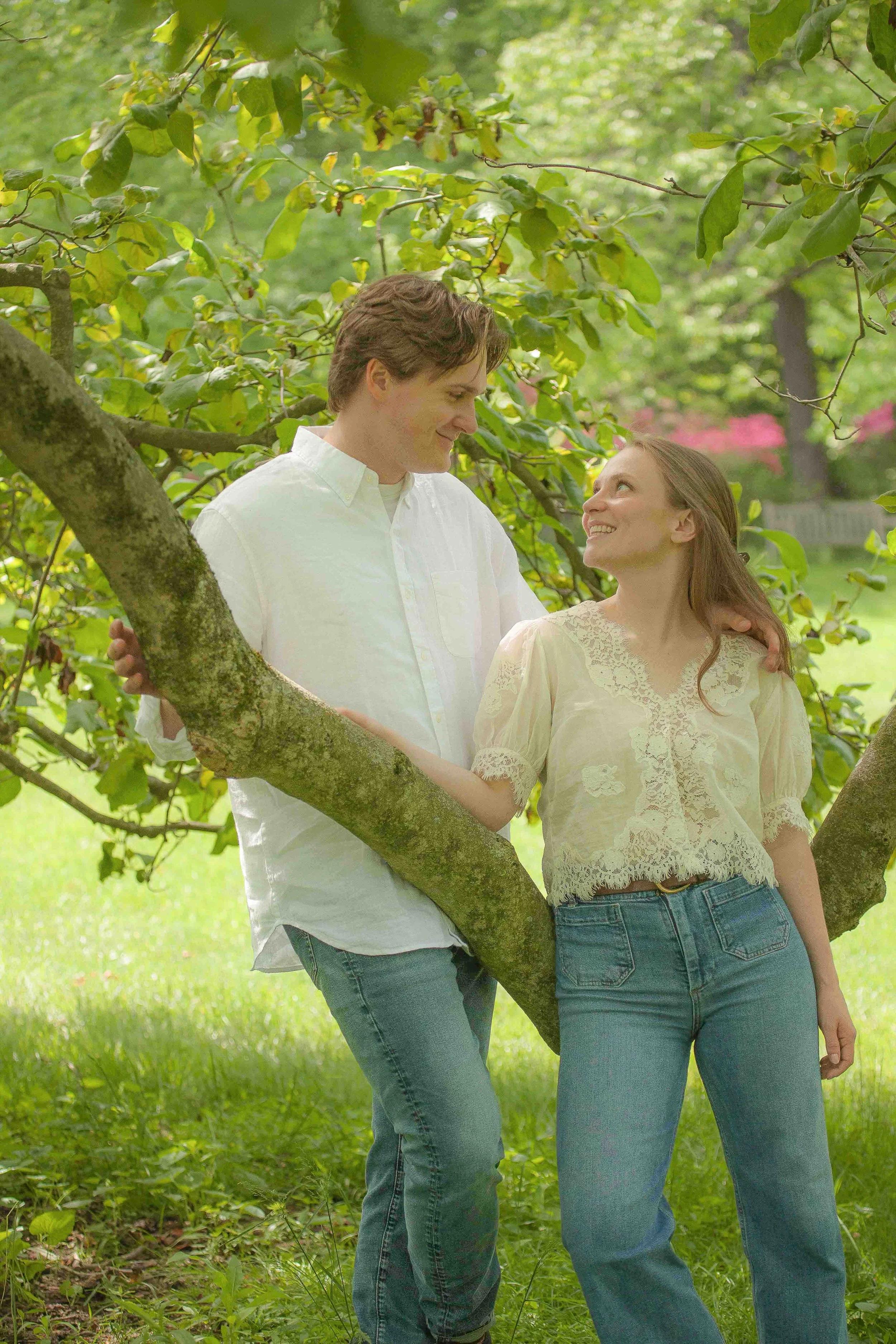 Engaged couple standing under a flowering tree at Winterthur, smiling at each other, the woman resting her hand on the man's arm.