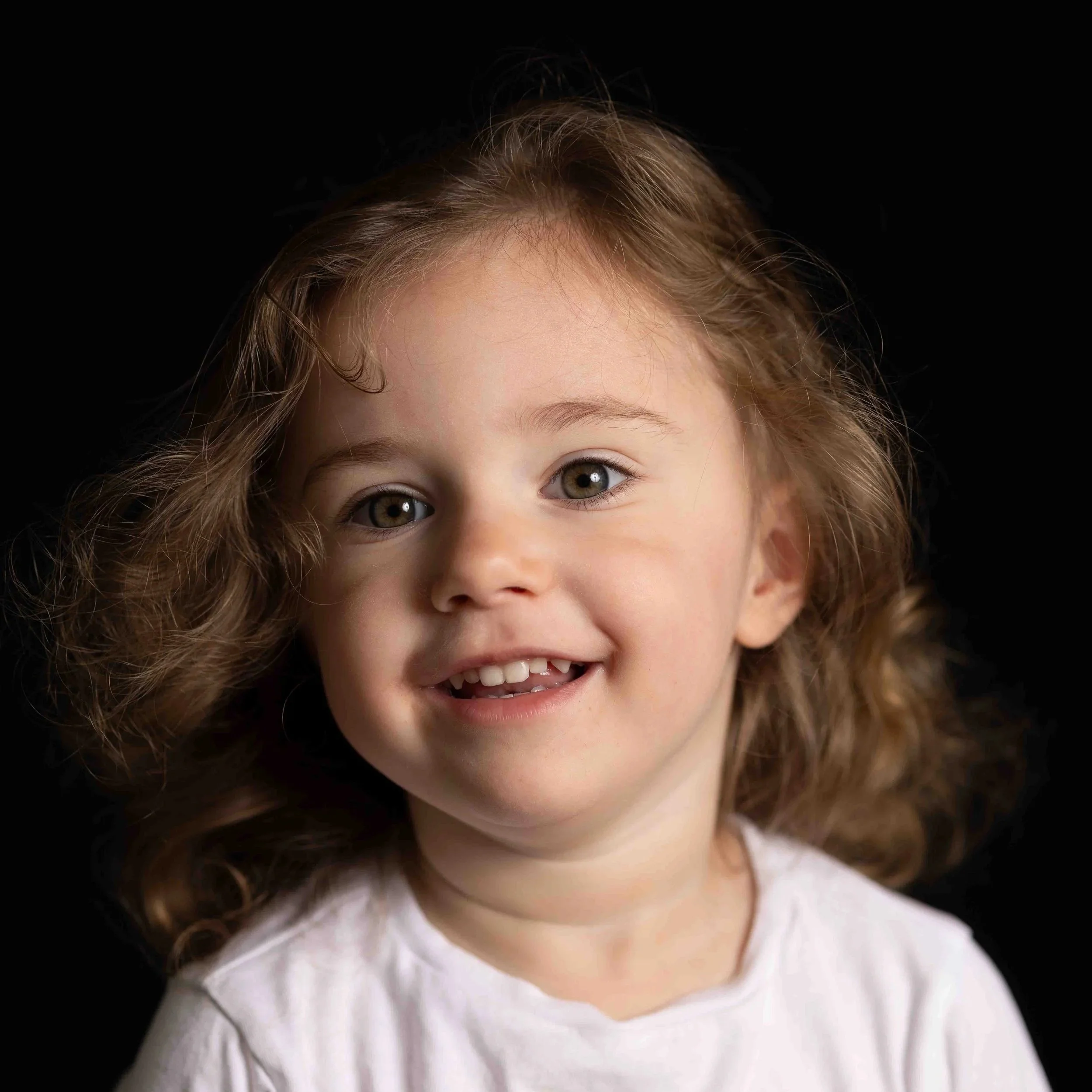 Little girl with light brown curly hair and brown eyes smiling for her preschool photo