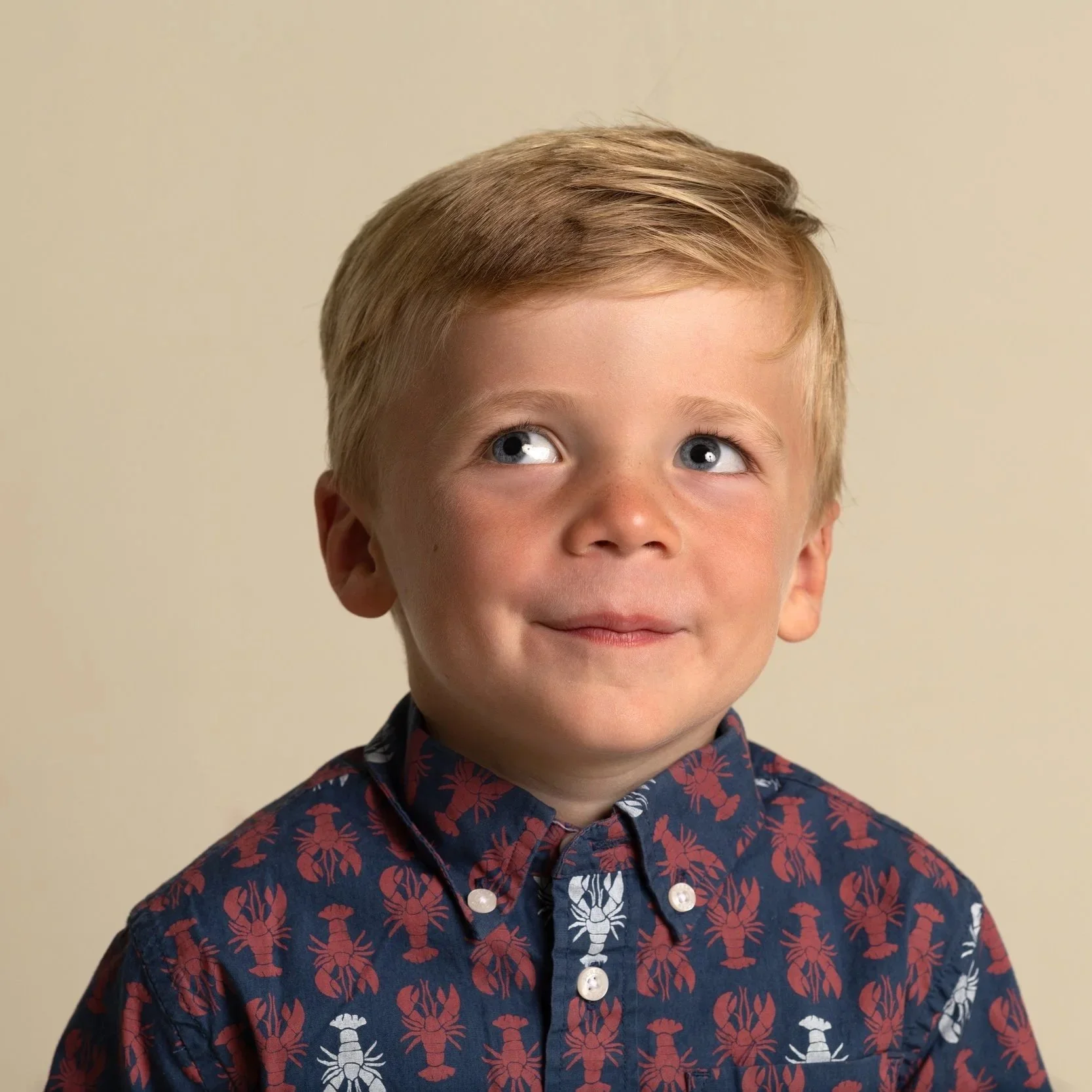 Little boy with short blond hair smiling and looking up and to his right for his preschool photo