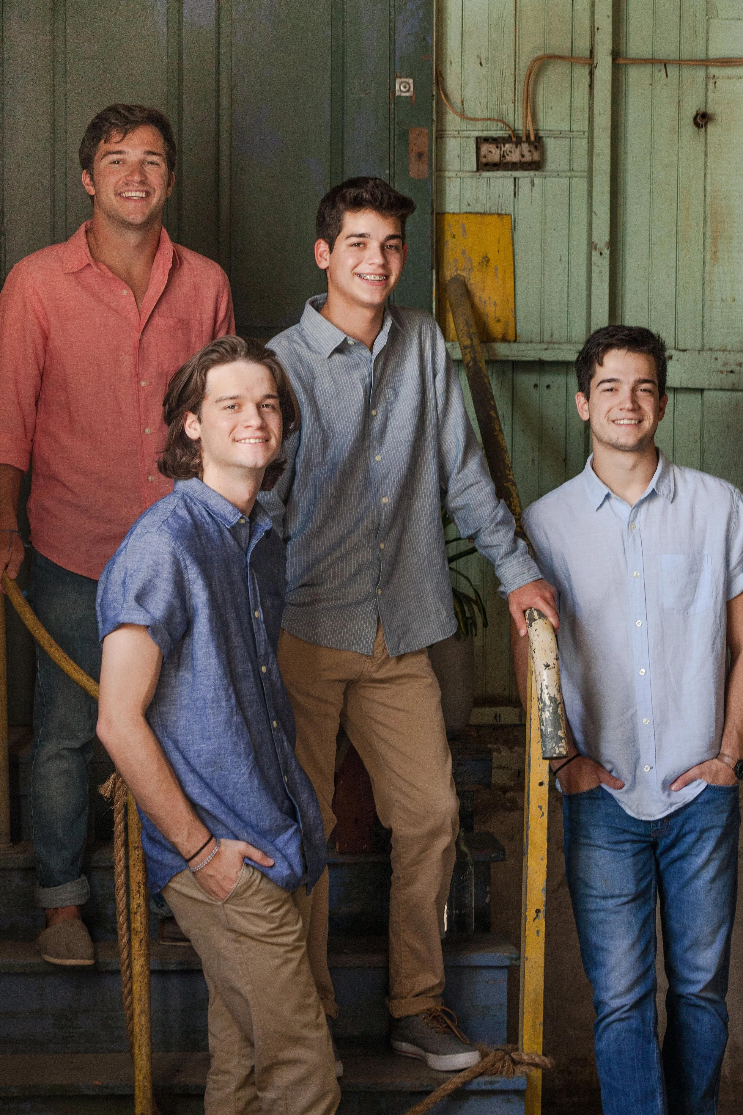 Four brothers laughing together against a weathered teal door, natural light lifestyle family portrait