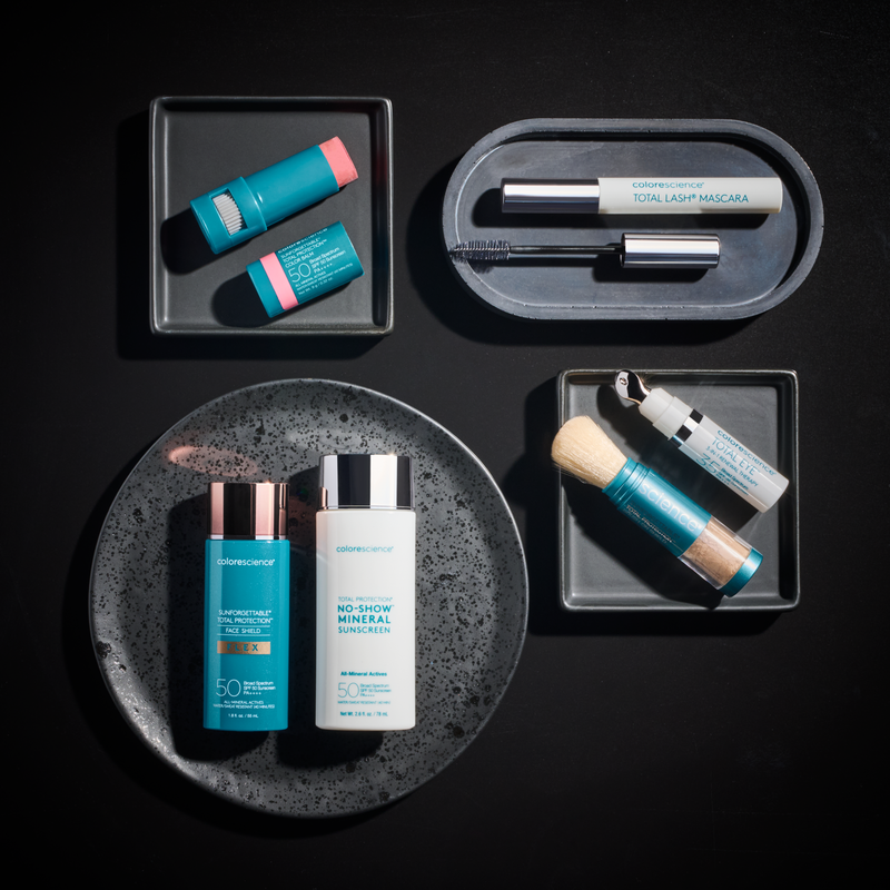 Skincare and beauty products including sunscreen, mascara, and a makeup brush on black trays and a black speckled plate.