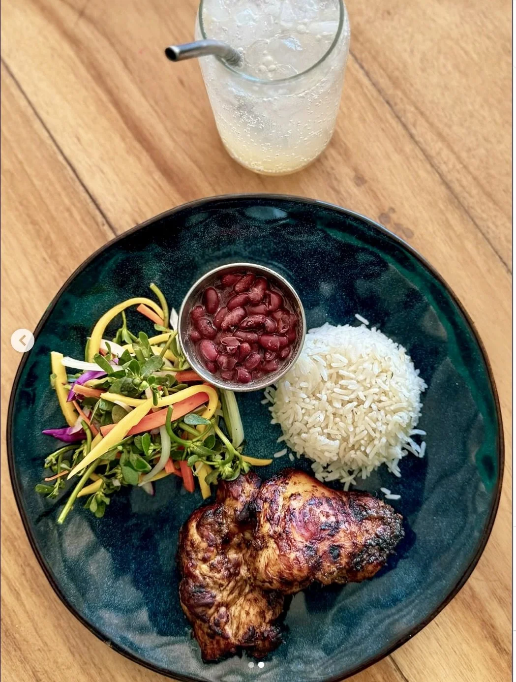 Plate with grilled chicken, white rice, bean salad, and a side of vegetables. Glass of soda with ice and a straw.